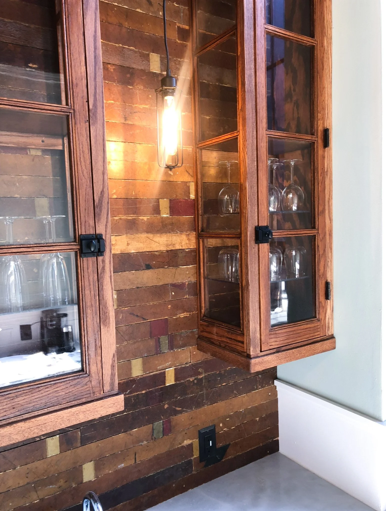 Salvaged gym floor planks repurposed as accent wall behind vintage glass cabinet in break room remodel