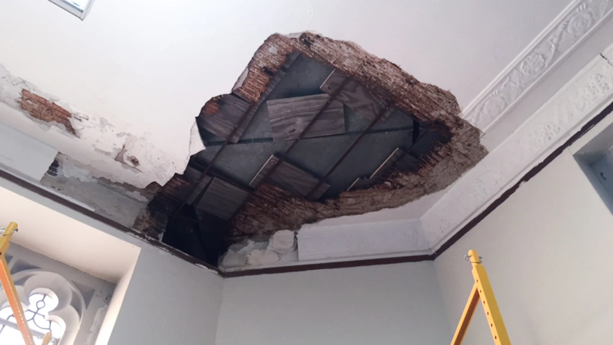 Large hole in plaster ceiling exposing wooden lath and joists after water damage