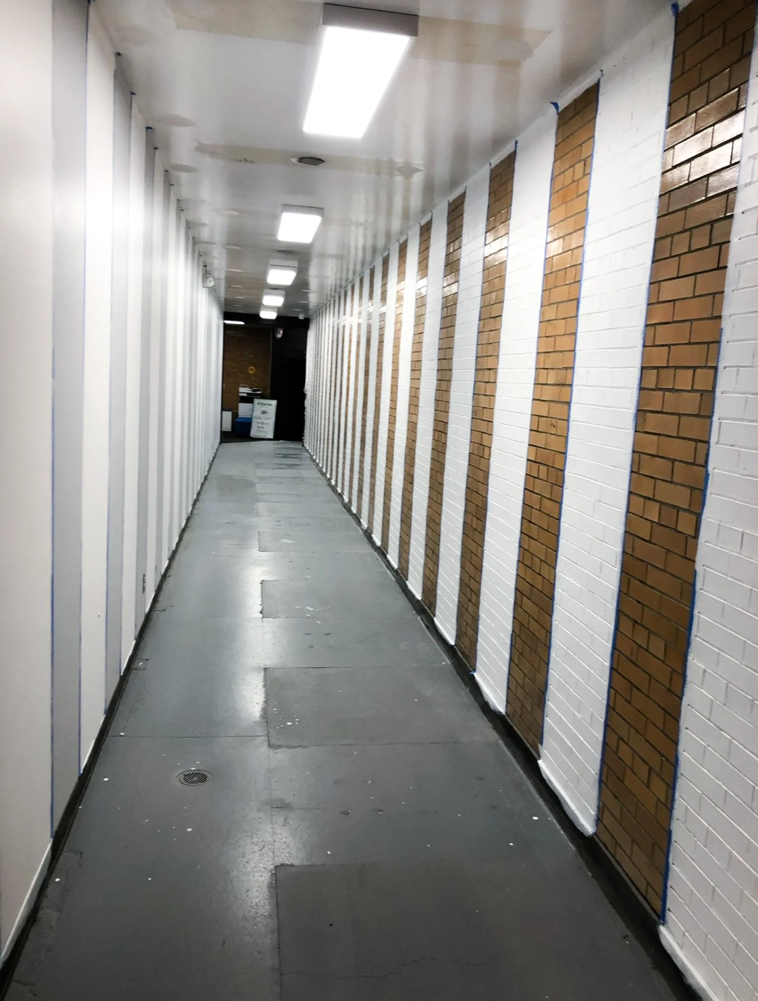 Narrow hallway with alternating white and bare brick stripes before mural installation