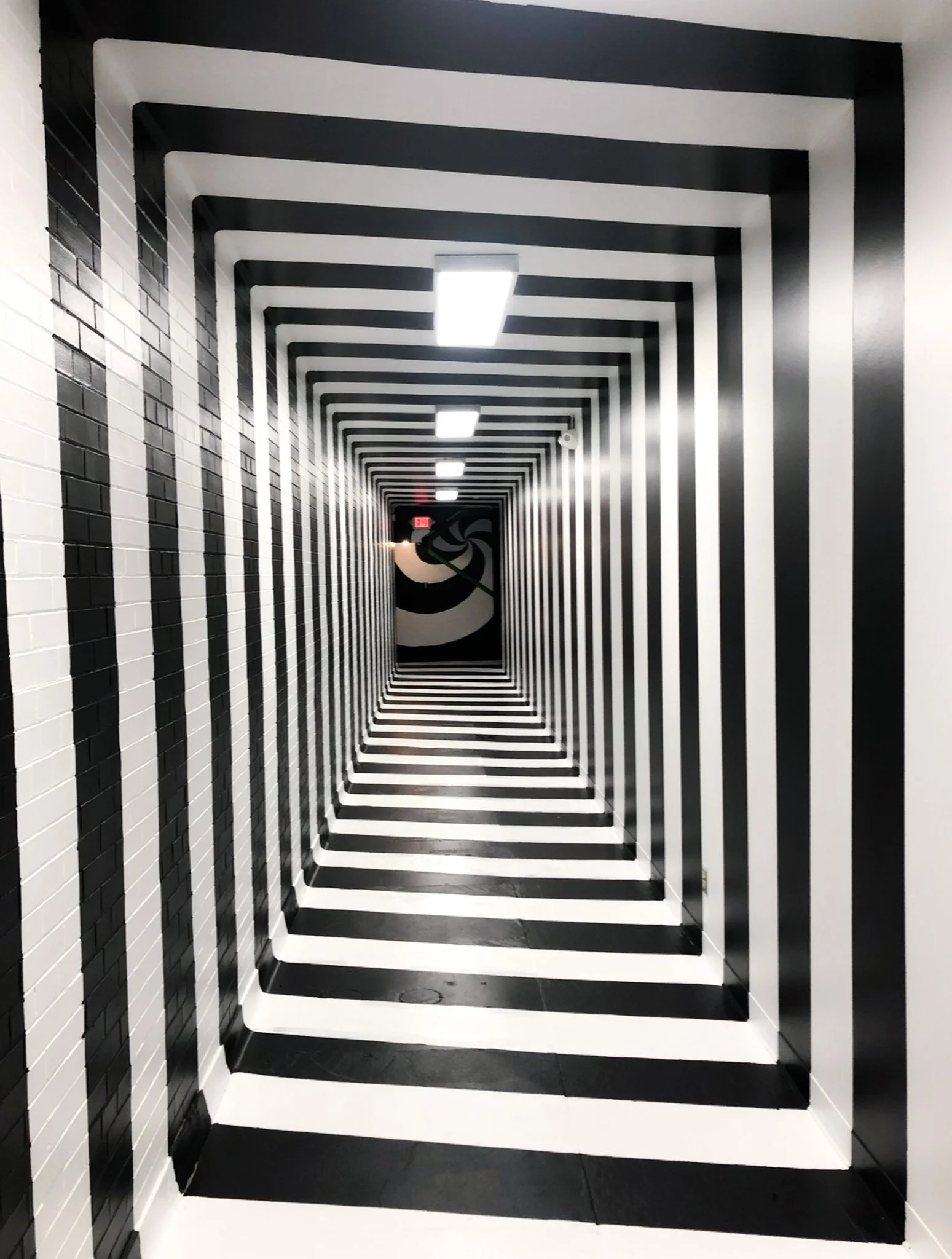 Hallway transformed with a black‑and‑white spiral mural creating a geometric tunnel effect