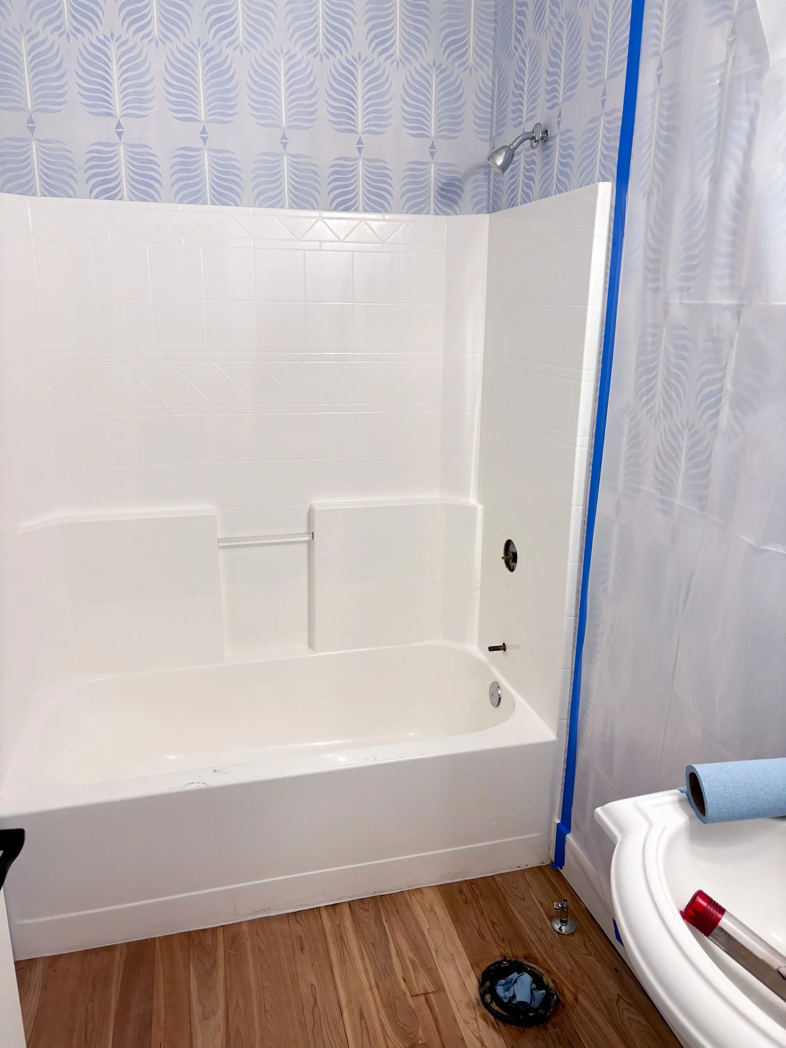 Outdated fiberglass shower/tub with white walls and painter’s tape around edges during remodel prep in Eagle, Idaho