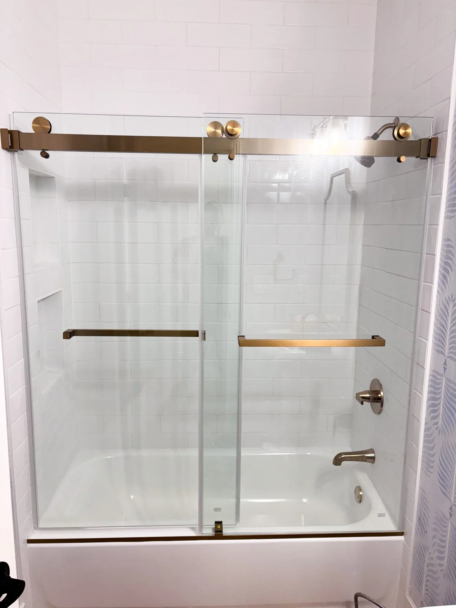 Completed shower remodel featuring tiled tub surround, niches and glass doors with brass hardware in Eagle, Idaho
