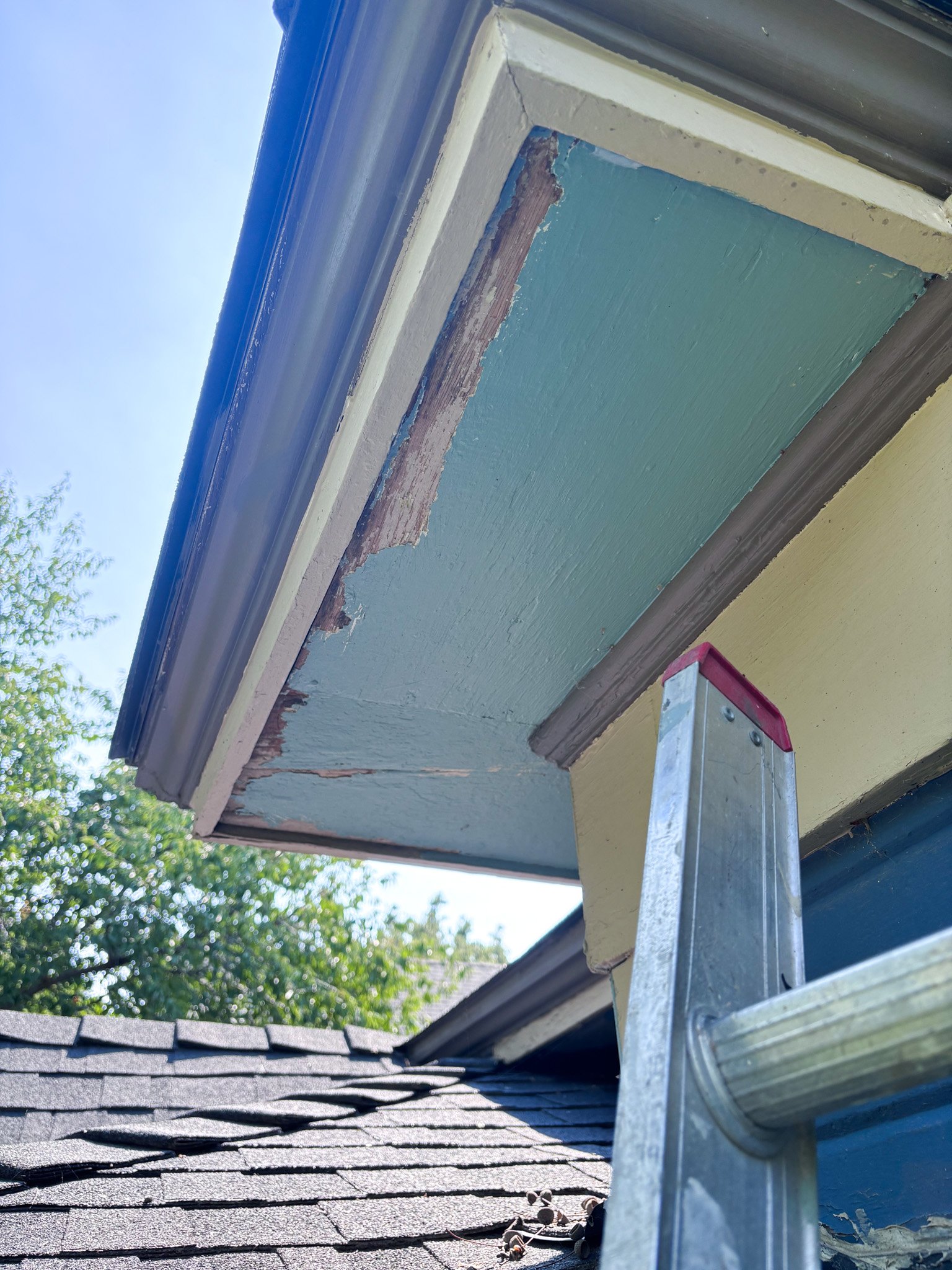 Under‑eave view showing decayed fascia and gutter damage before repair, ladder in place, Garden City, Idaho