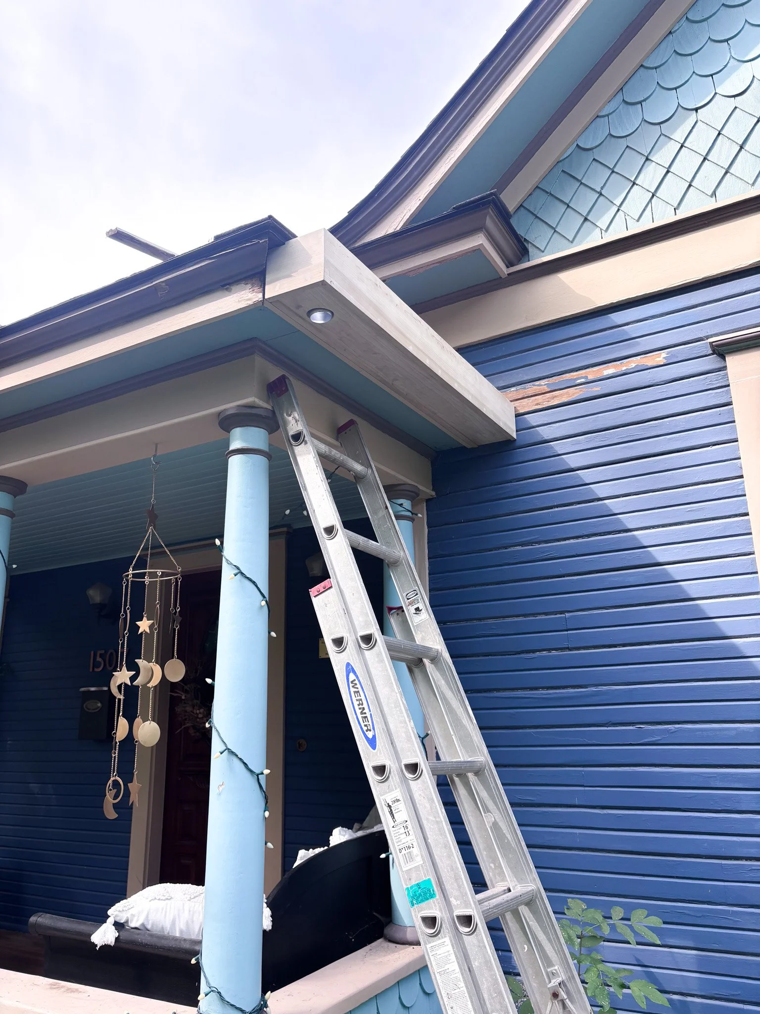 Hidden gutter trough being installed along front porch roofline with ladder and tools