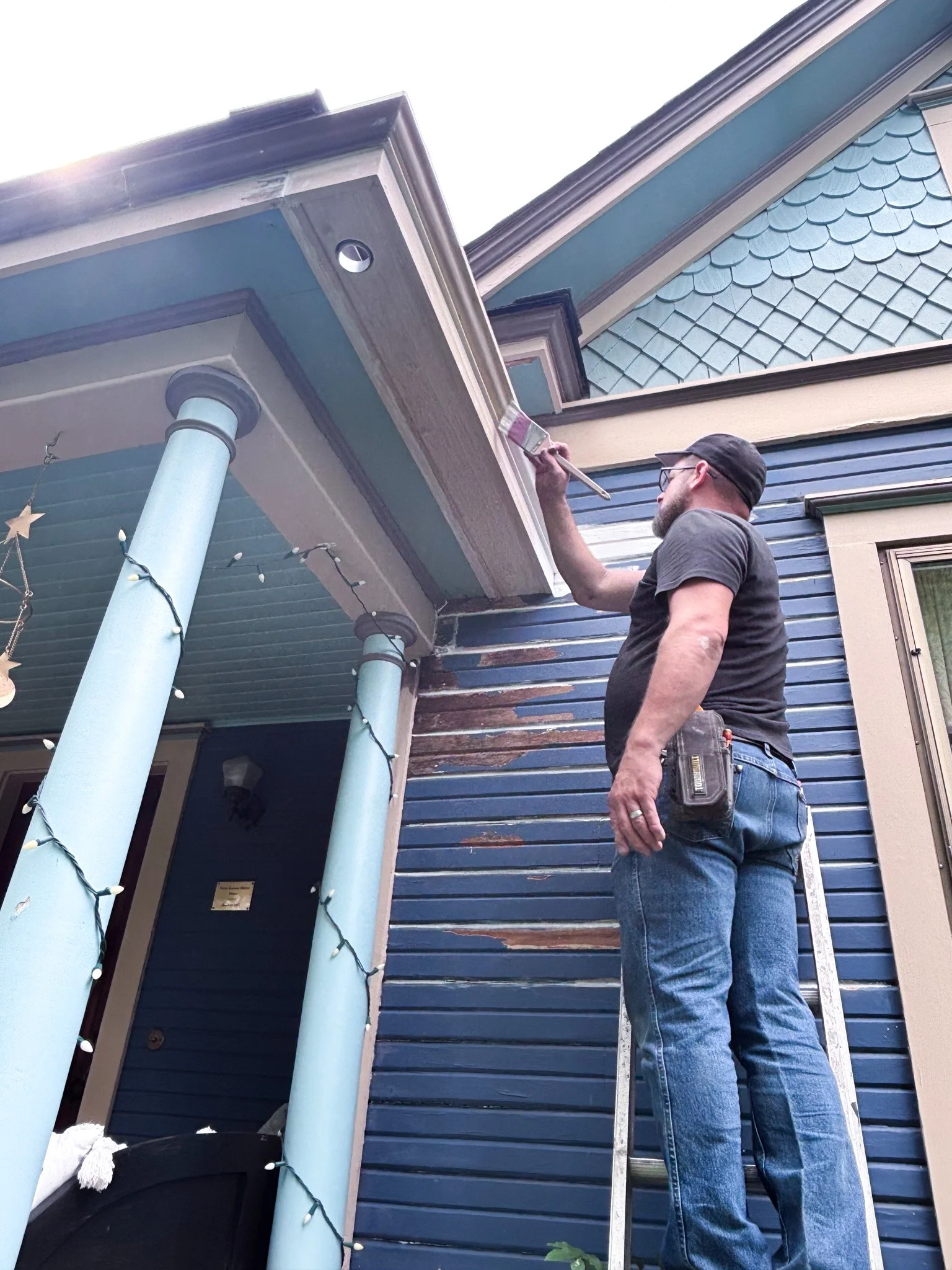 Jake painting installed hidden gutter trim while on a ladder in Garden City, Idaho
