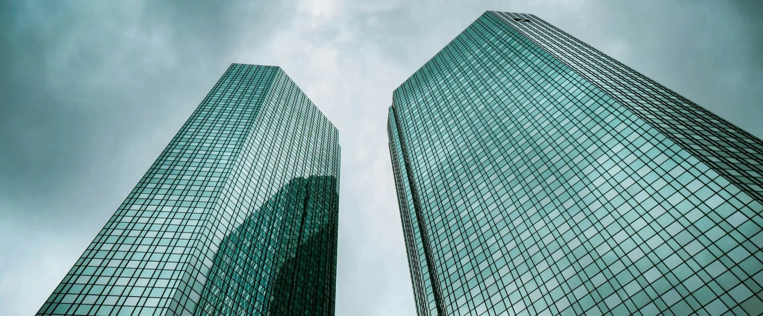 Two modern glass skyscrapers viewed from the ground looking up against a cloudy sky.