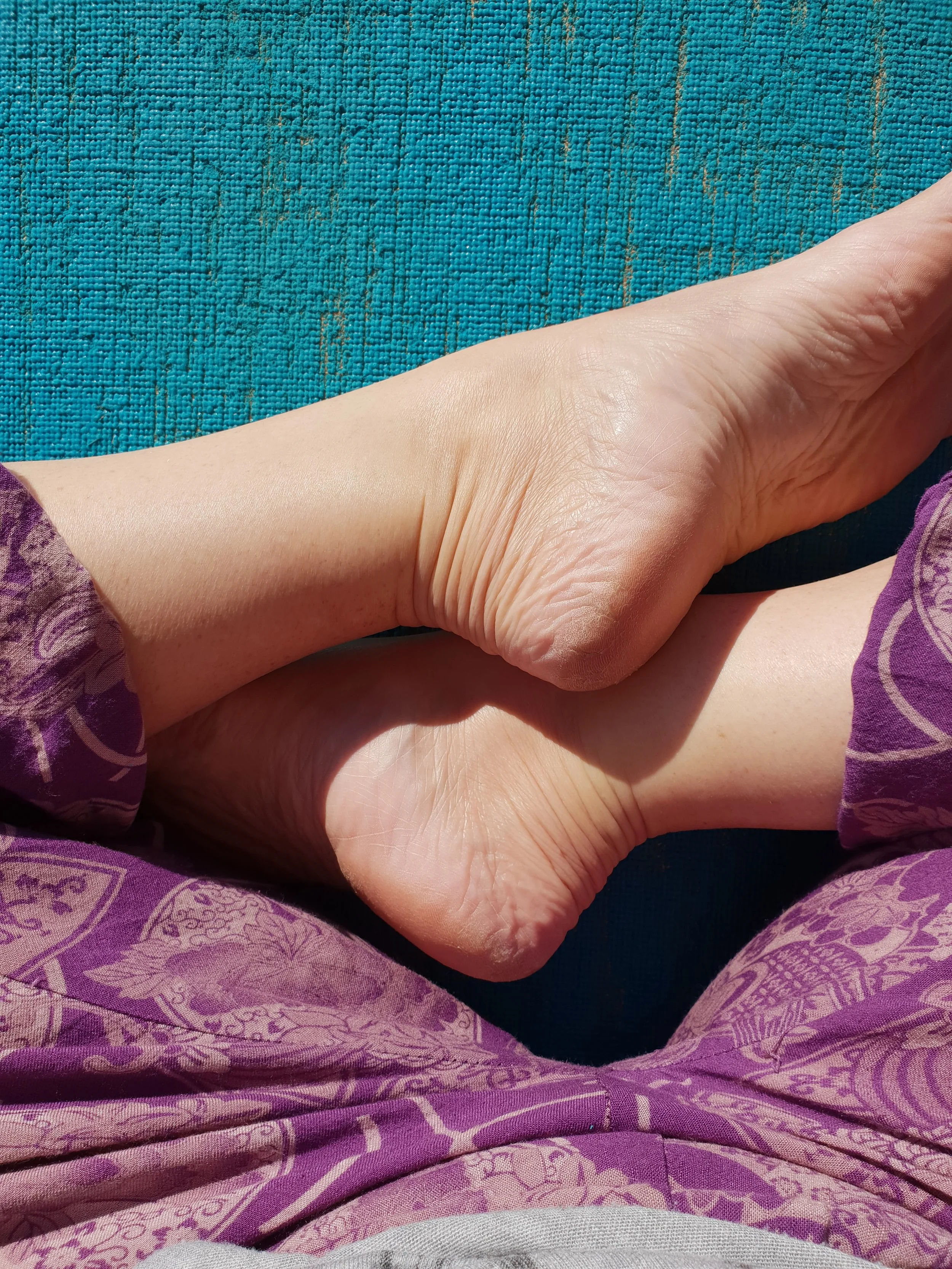 Close-up of two hands, one gently holding the other, with purple patterned clothing visible on the person's wrist, against a blue textured background.