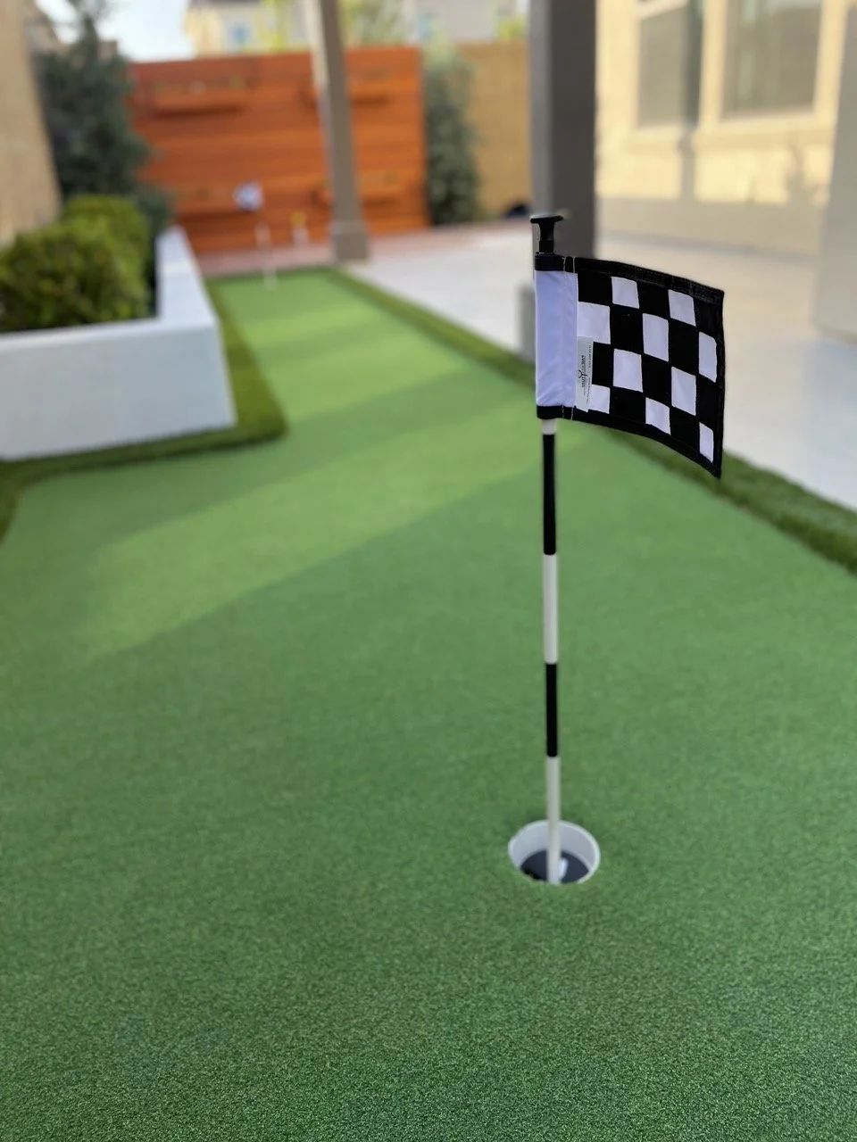 Mini golf green with flag in hole, on a backyard patio.