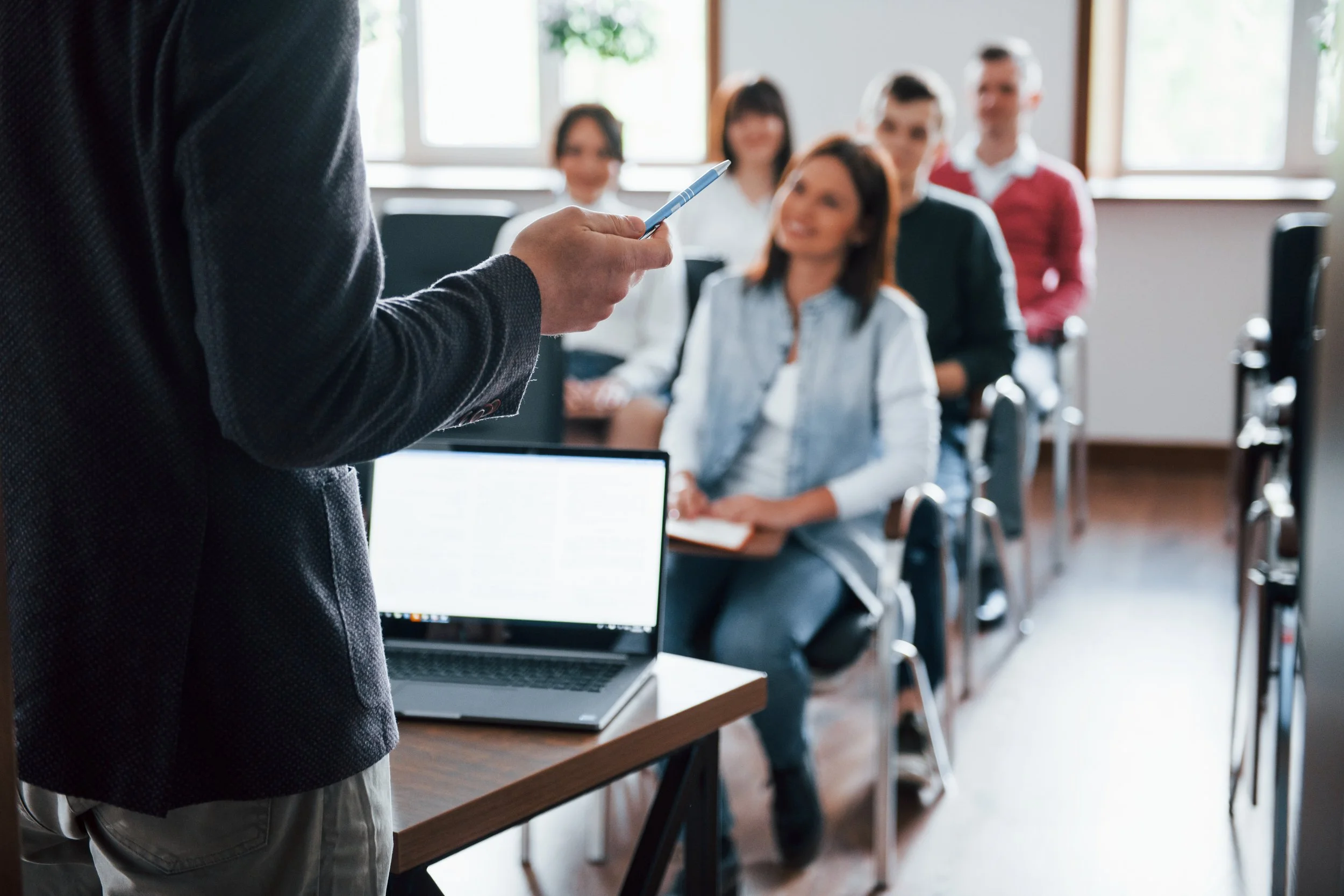 Person giving a presentation in front of a group of attentive audience members in a classroom or conference room.