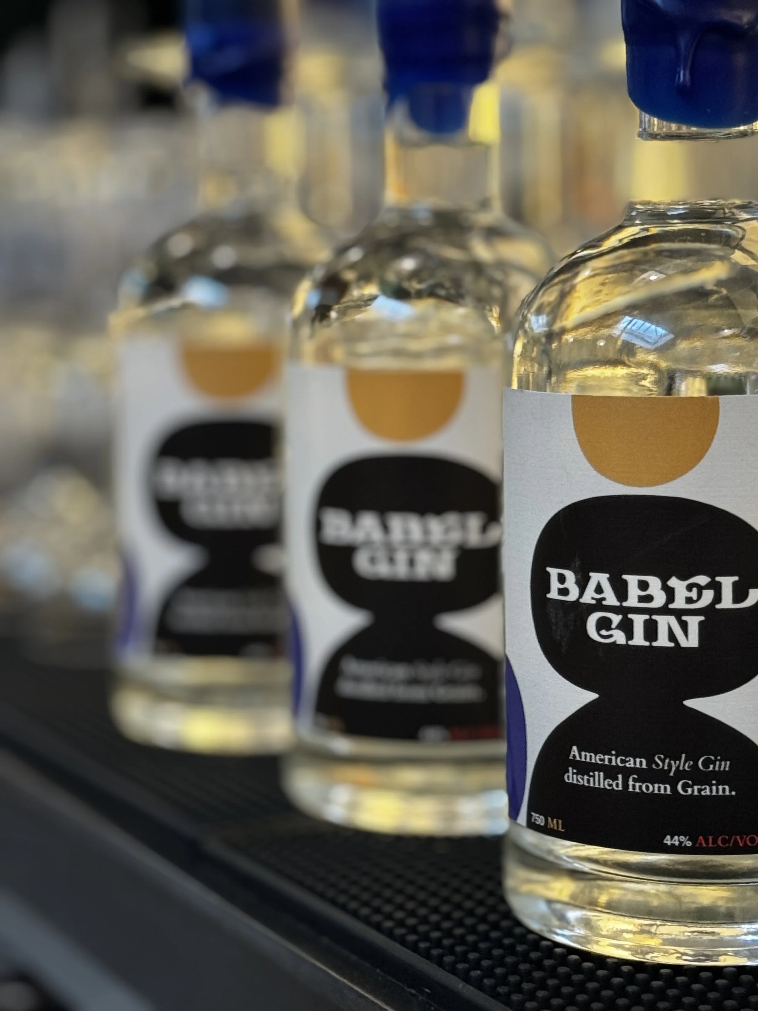 Close-up of multiple bottles of Babel Gin with black, white, and gold labels on a display shelf.