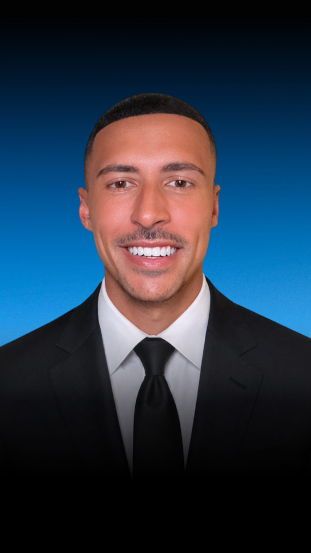 Portrait of a man in a suit and tie smiling, with a blue gradient background.