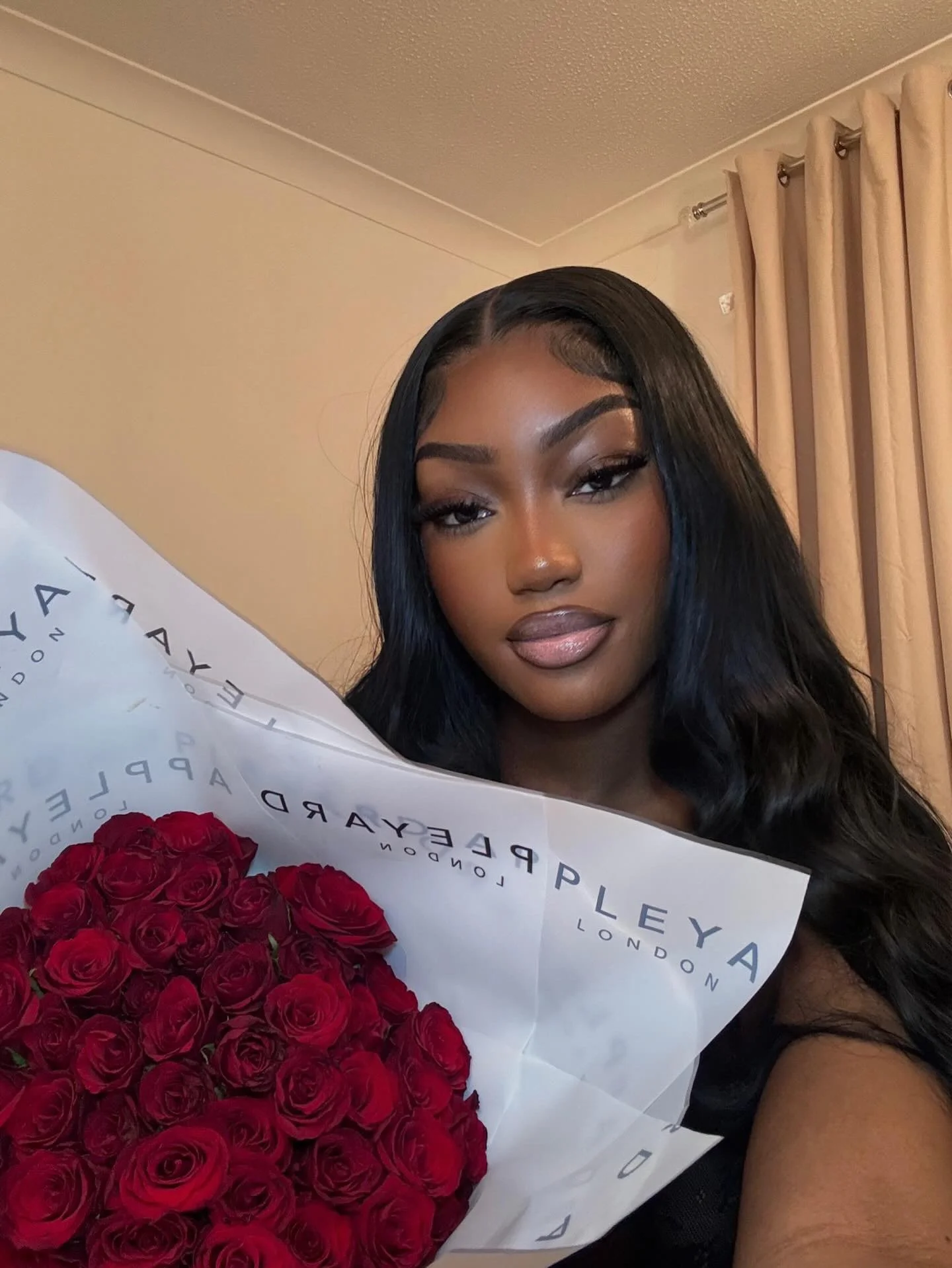 Woman with long black hair holding a bouquet of red roses wrapped in white paper with blue text