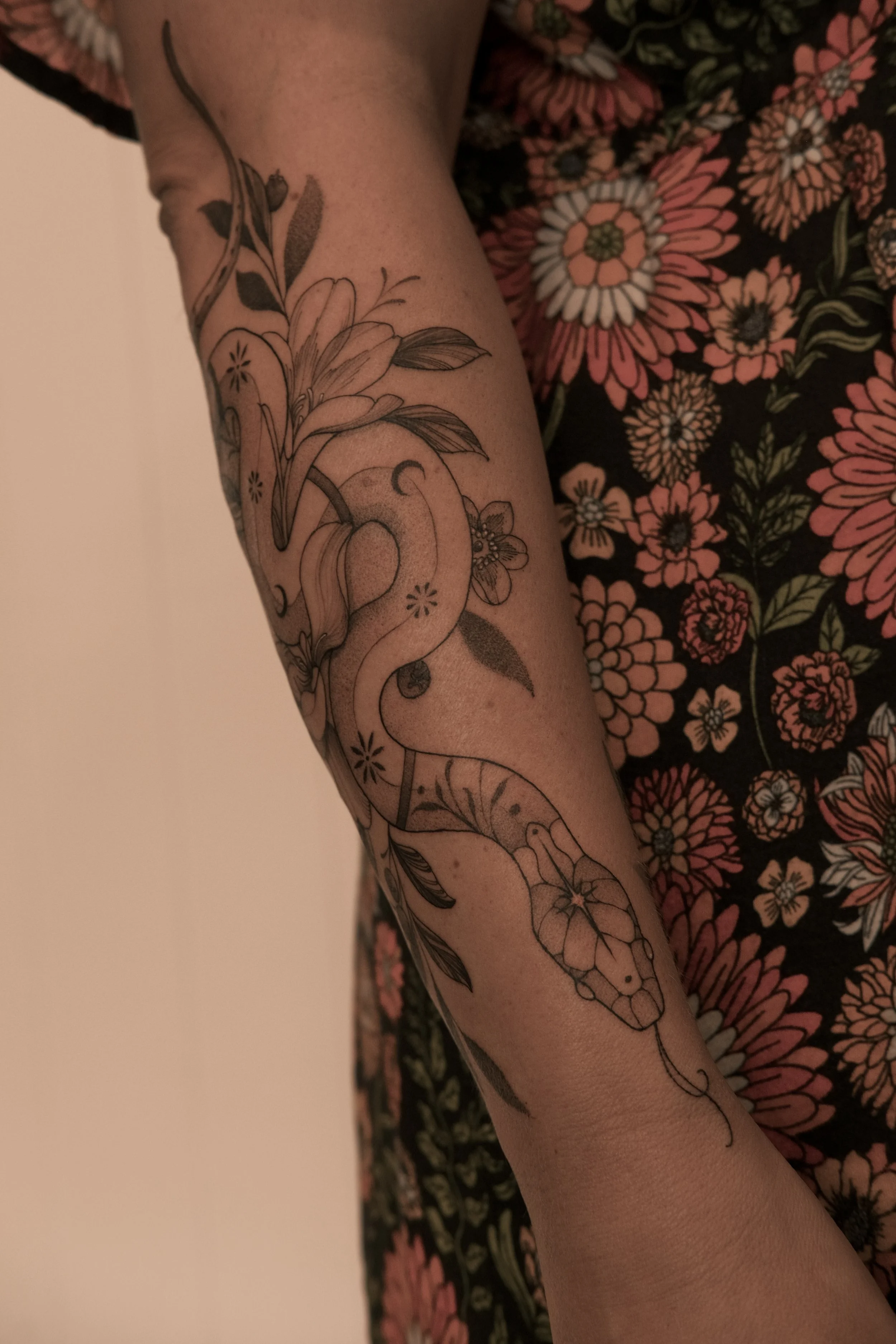 Nature-inspired tattoo featuring a snake, wildflowers and botanical details in fine line blackwork.