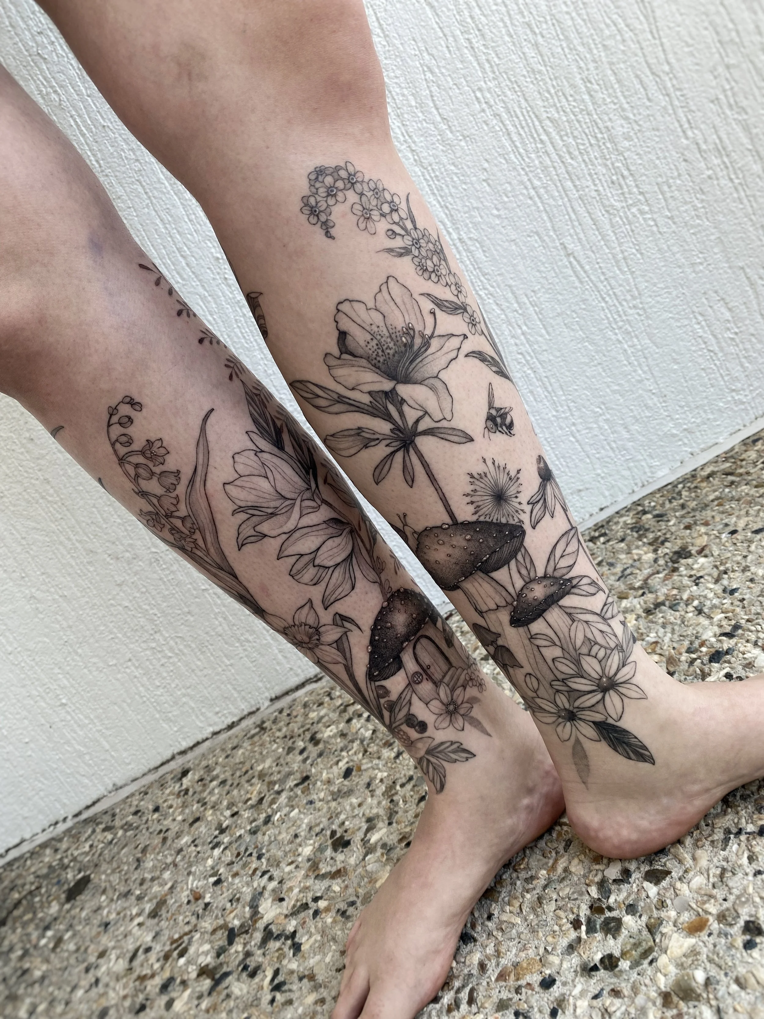 Botanical leg and foot tattoos featuring wildflowers, foliage, and fine line blackwork.