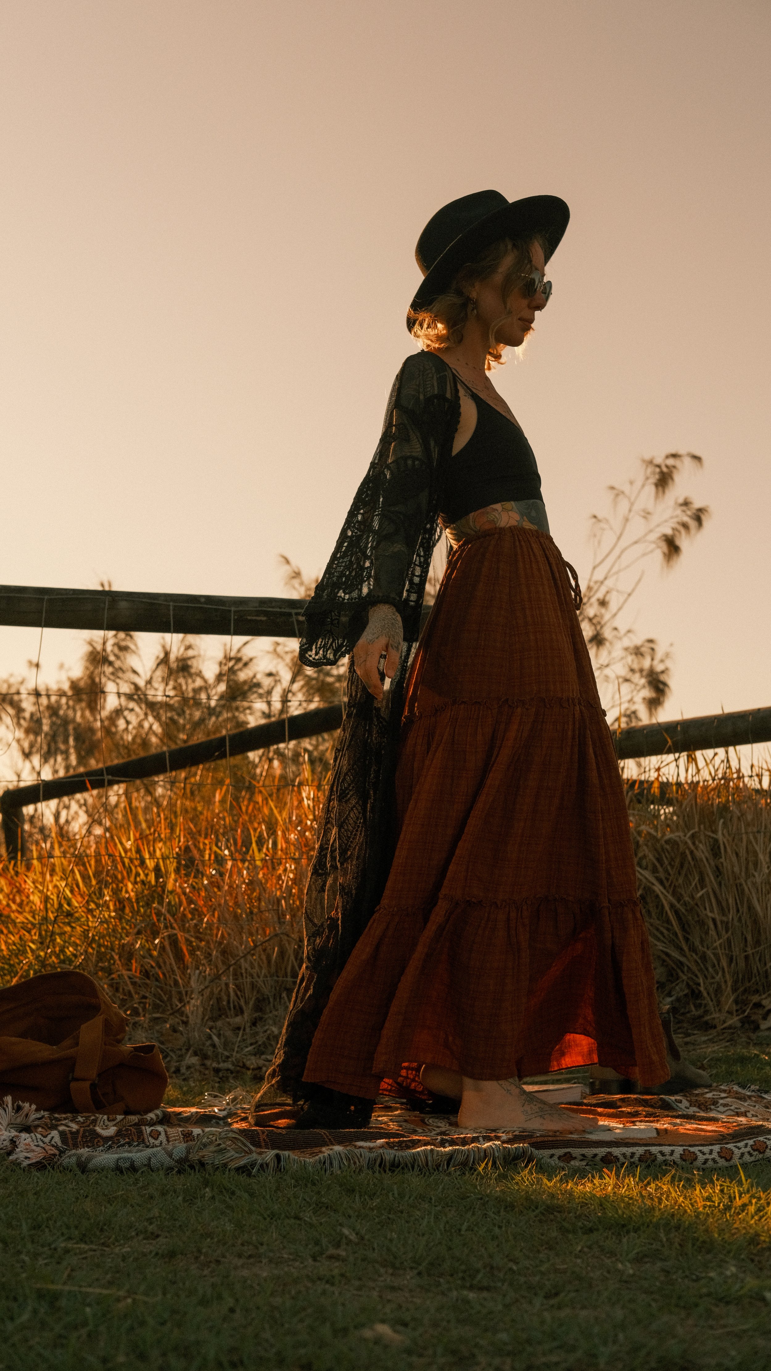 Artist standing in a sunlit field at golden hour, surrounded by tall grasses and warm evening light