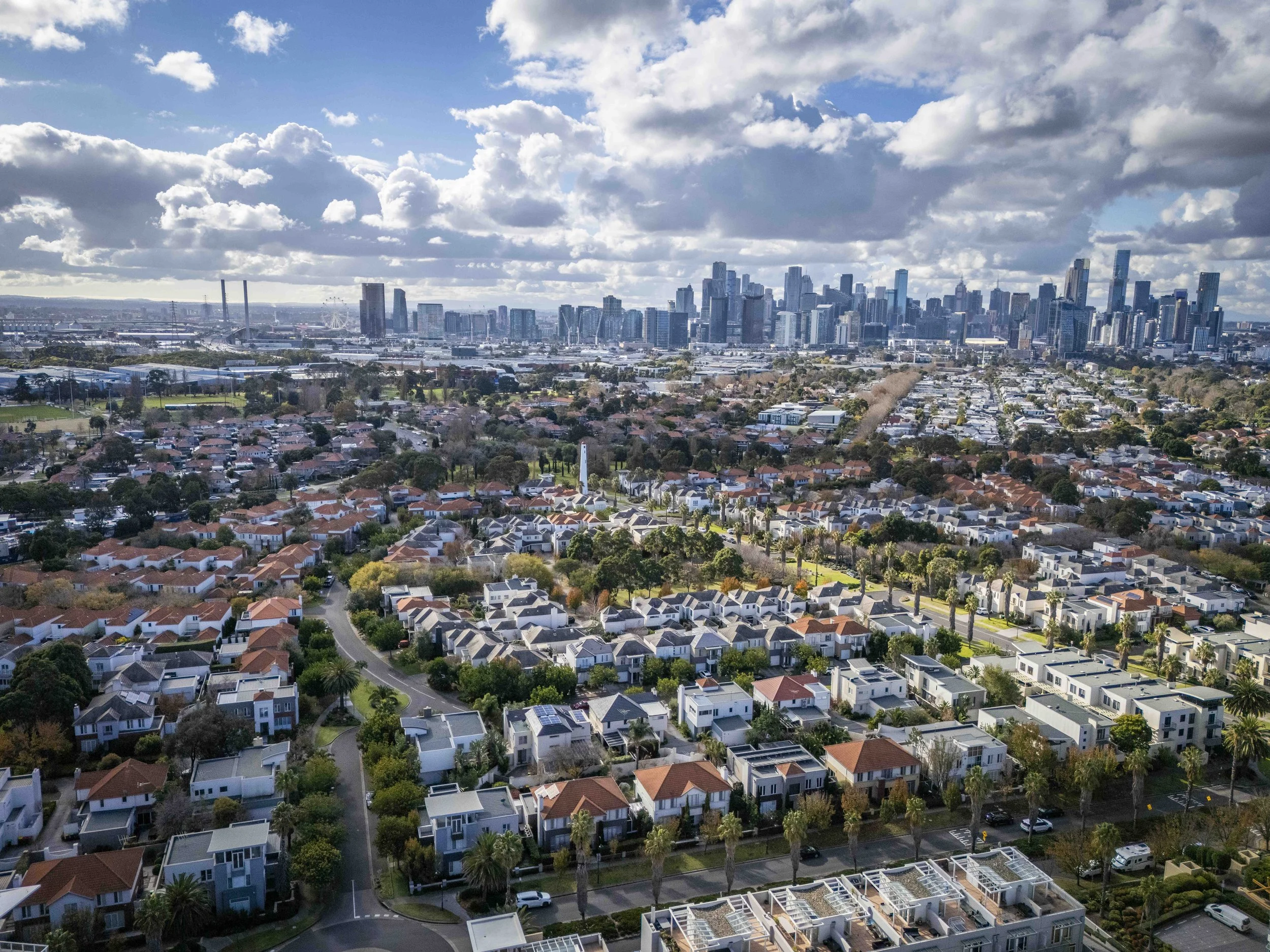 Aerial view of a residential neighborhood with a city skyline and tall buildings in the background, under a partly cloudy sky.