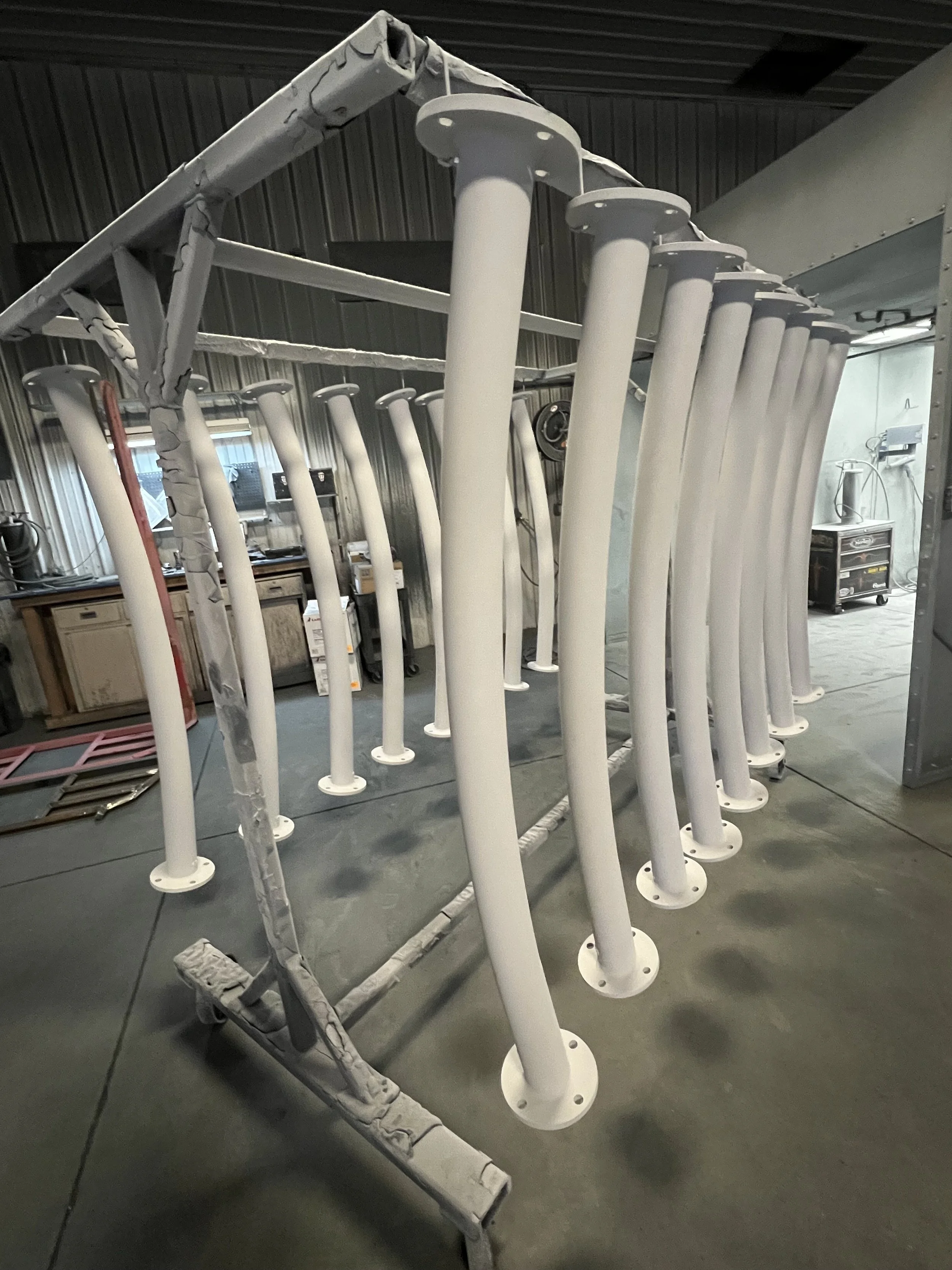 A metal framework with multiple white cylindrical pipes attached, situated in an industrial or workshop setting.