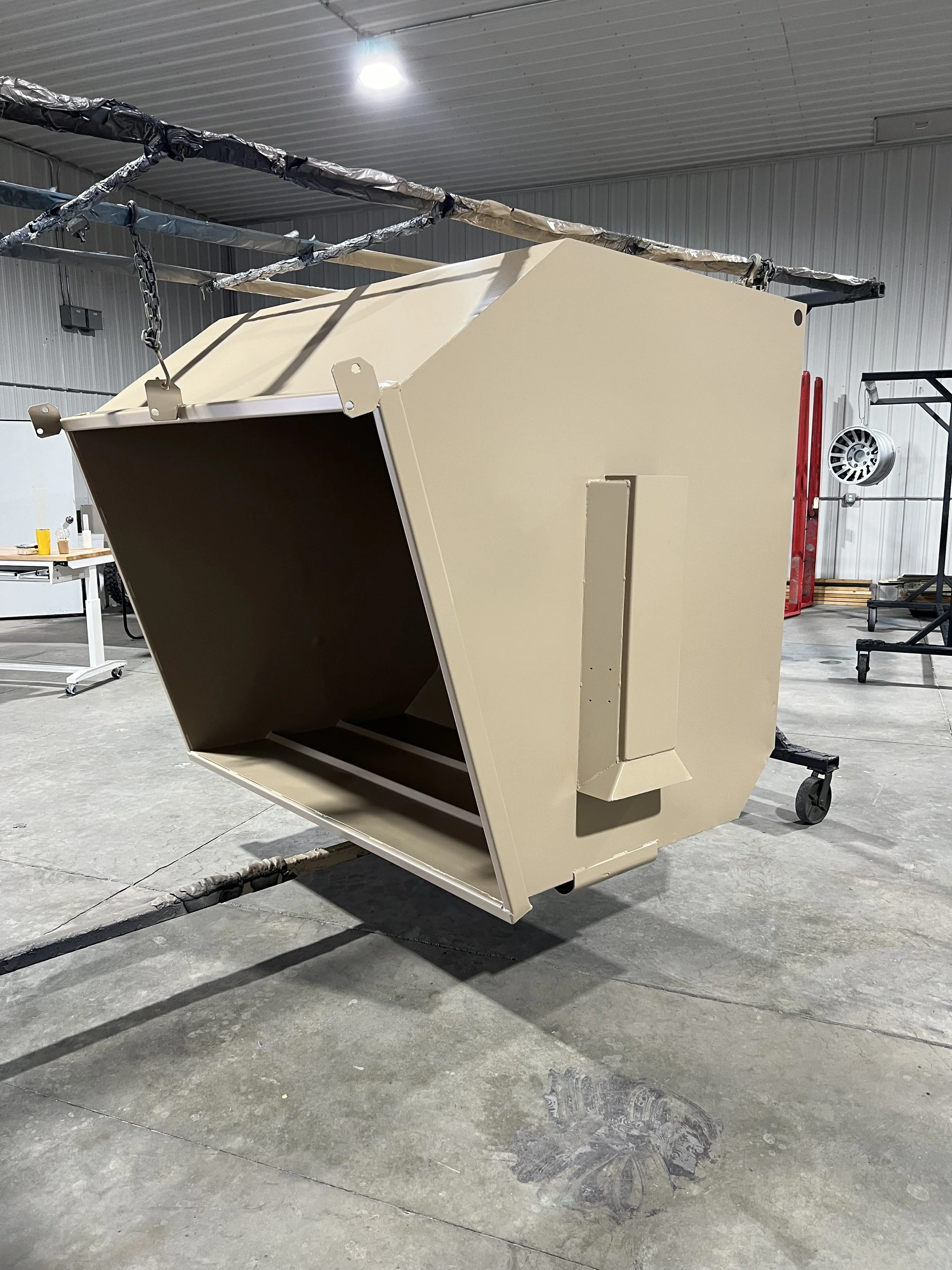 A beige industrial machine or component inside a warehouse, suspended by chains, with a dark interior and a rectangular shape.