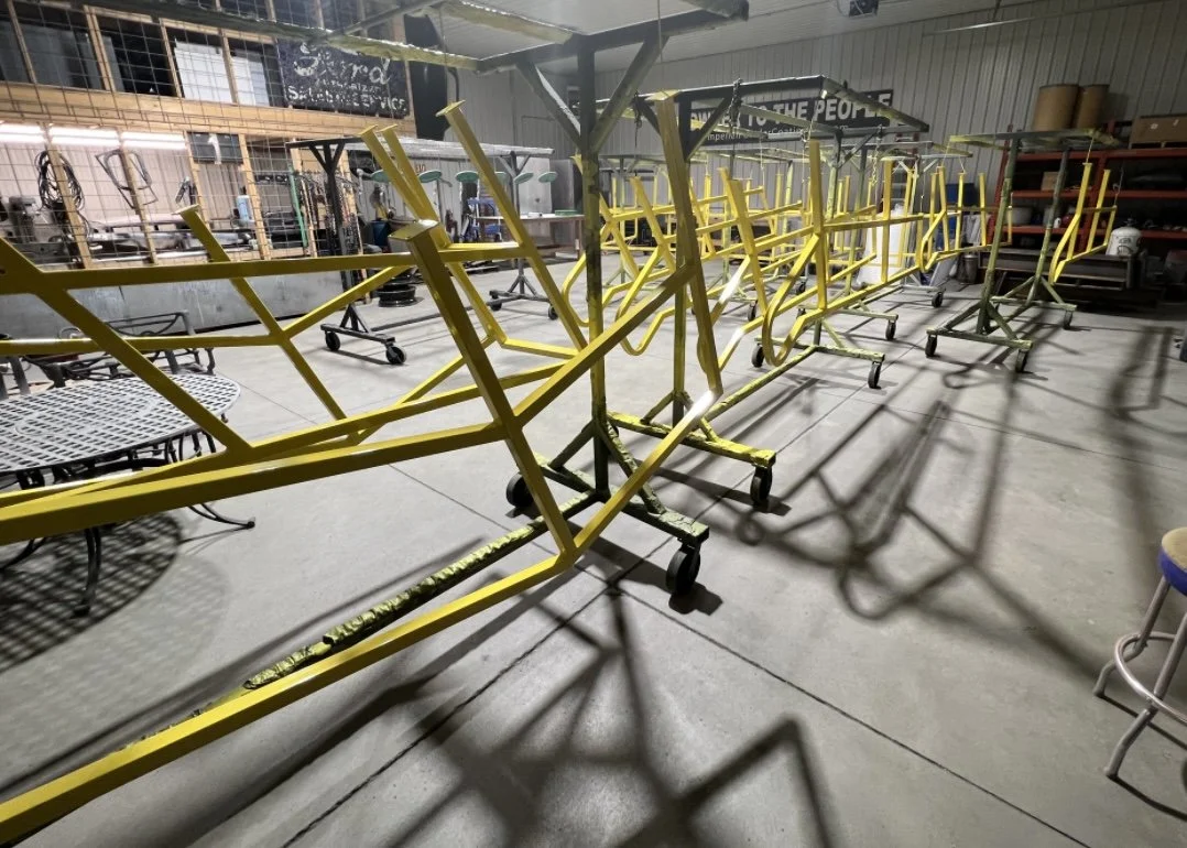 Multiple yellow and green metal rolling carts lined up inside a workshop or storage area with tools and shelves in the background.