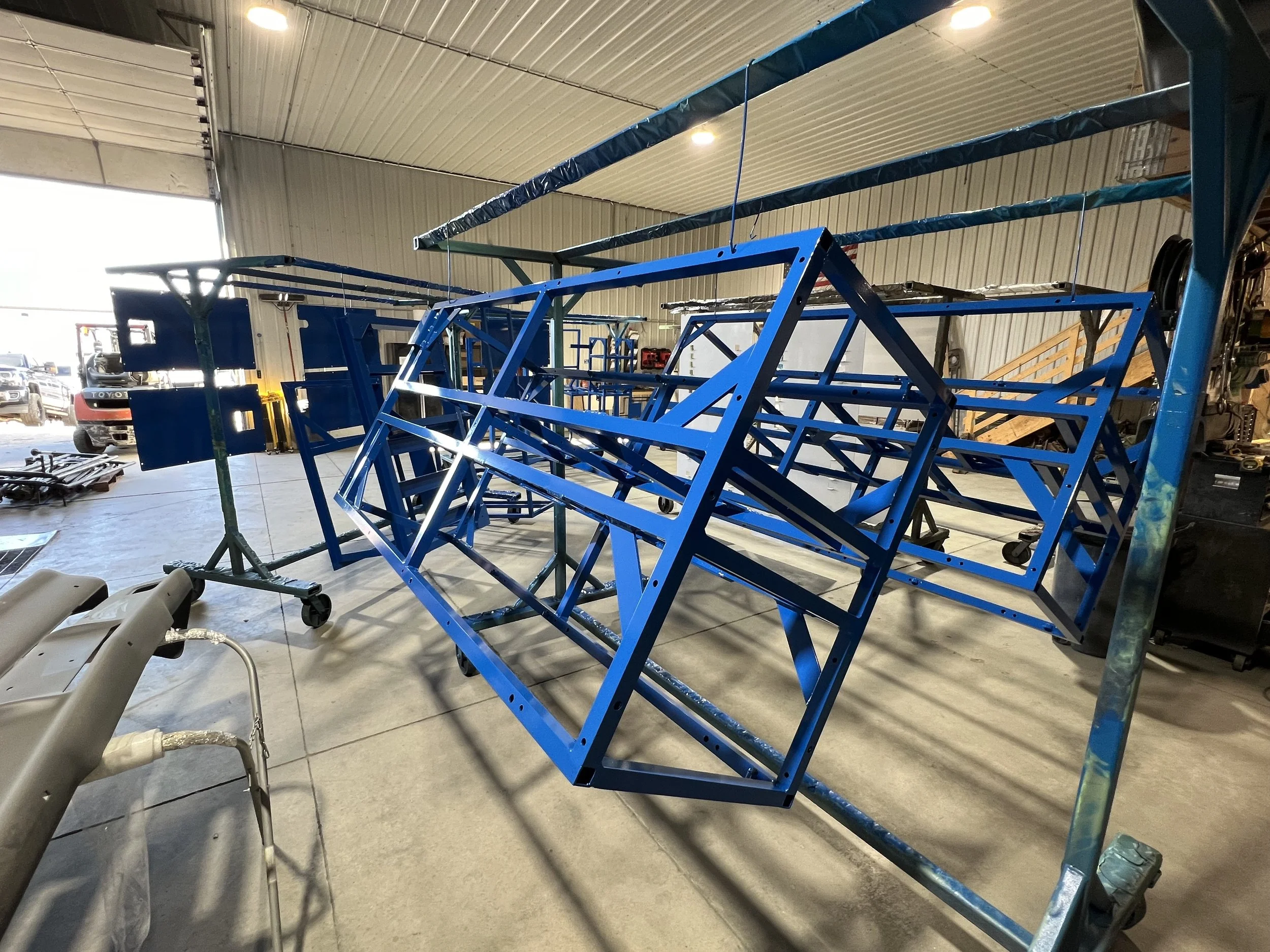 Blue metal framework structure inside a workshop, possibly part of a vehicle or equipment being assembled or repaired.