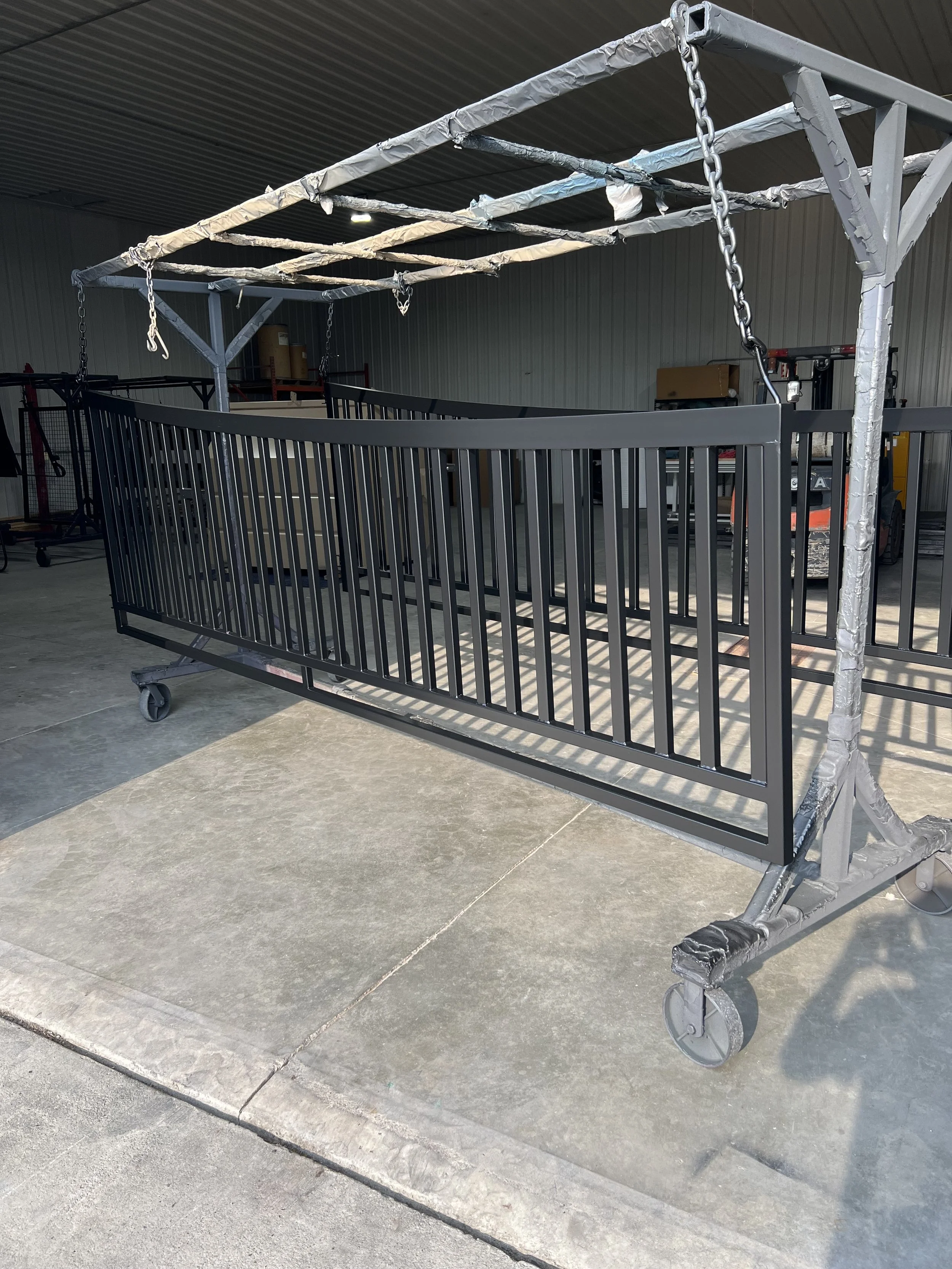 A black metal gate with vertical bars mounted on a mobile metal frame with wheels, inside an industrial warehouse.