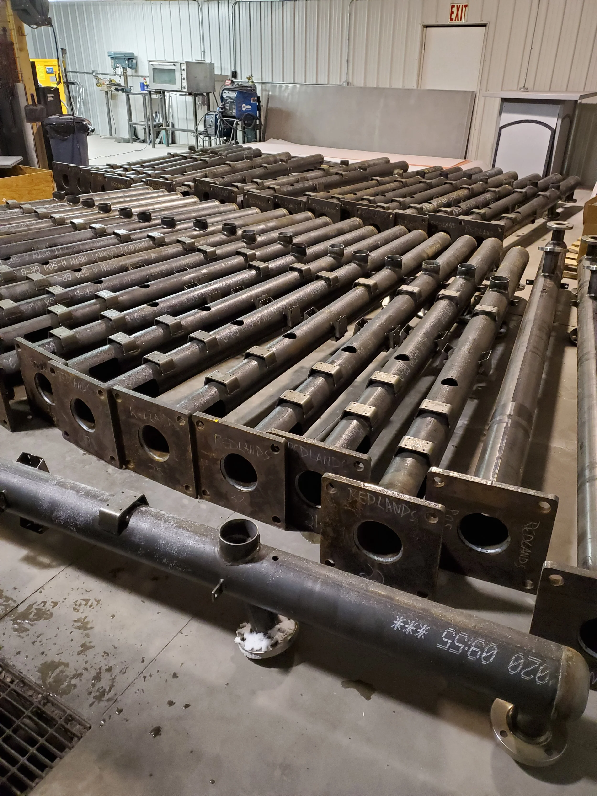 Multiple large metal pipes and cylindrical components arranged on wheeled carts inside an industrial workshop.
