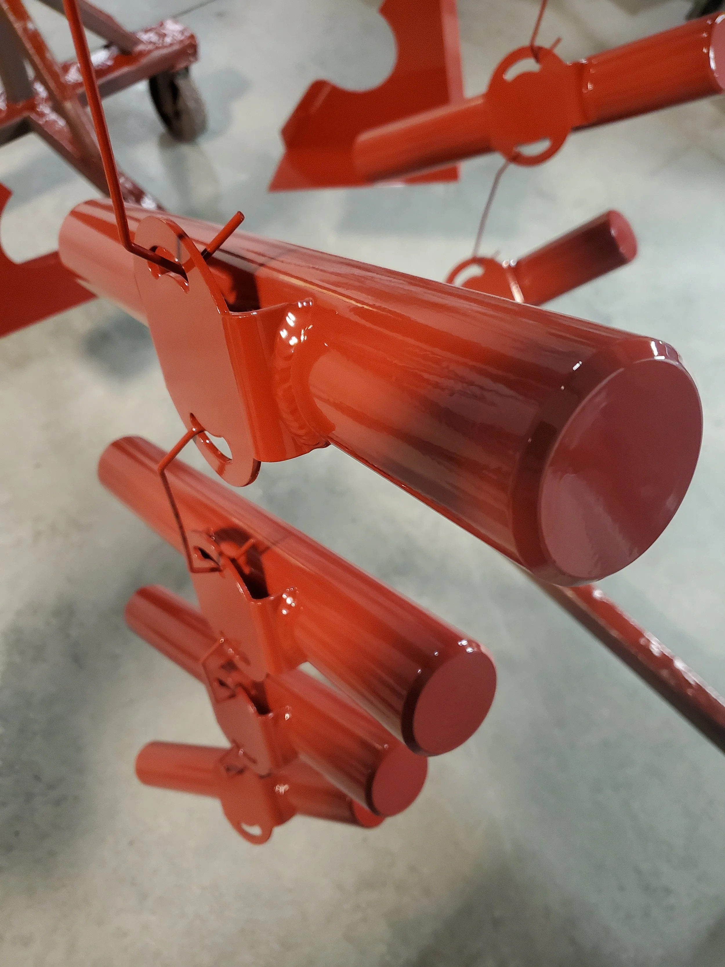 Close-up of red metal firework rockets hanging vertically from a metal frame, with a concrete floor in the background.