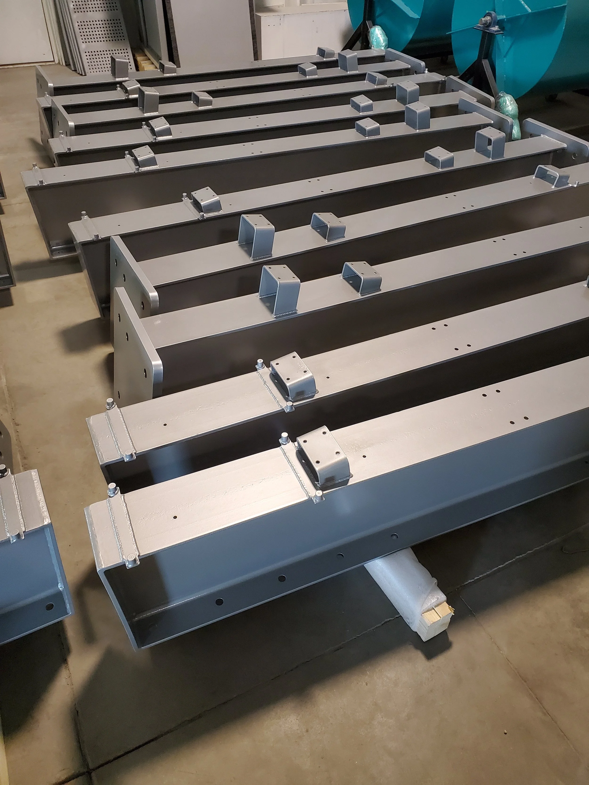 Several metal frame structures with brackets and bolts, stored on a pallet in an indoor warehouse.