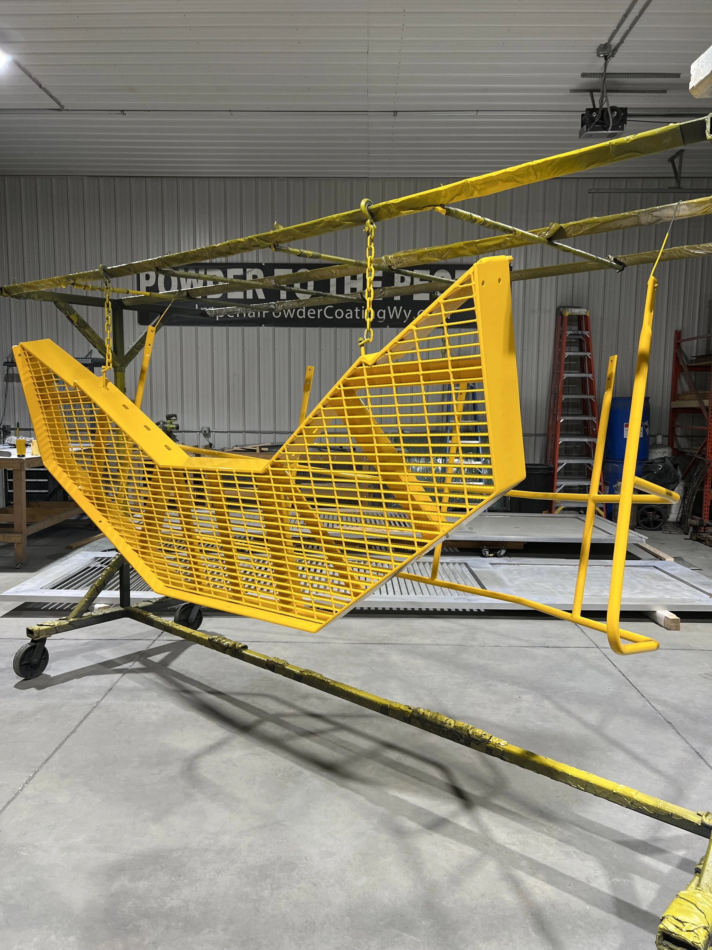 Yellow metal safety barrier with a chain hanging from the top, set inside a warehouse with industrial shelving and equipment in the background.