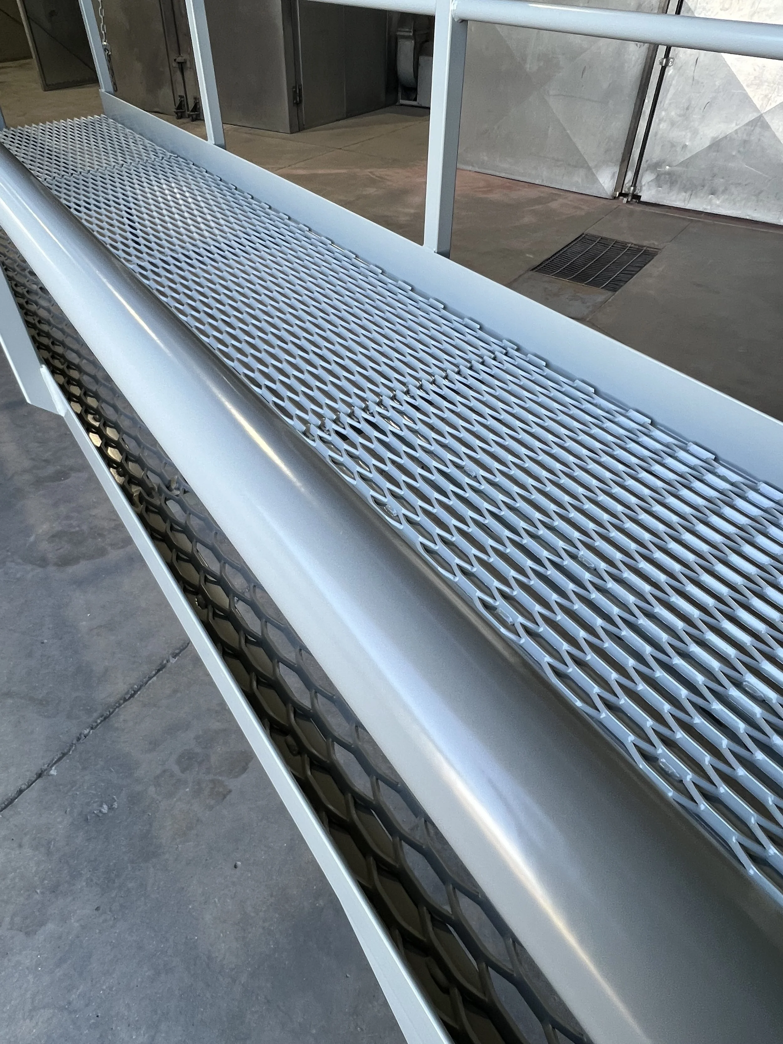 A metal walkway with a textured surface and a rounded handrail, located in an industrial or warehouse setting.
