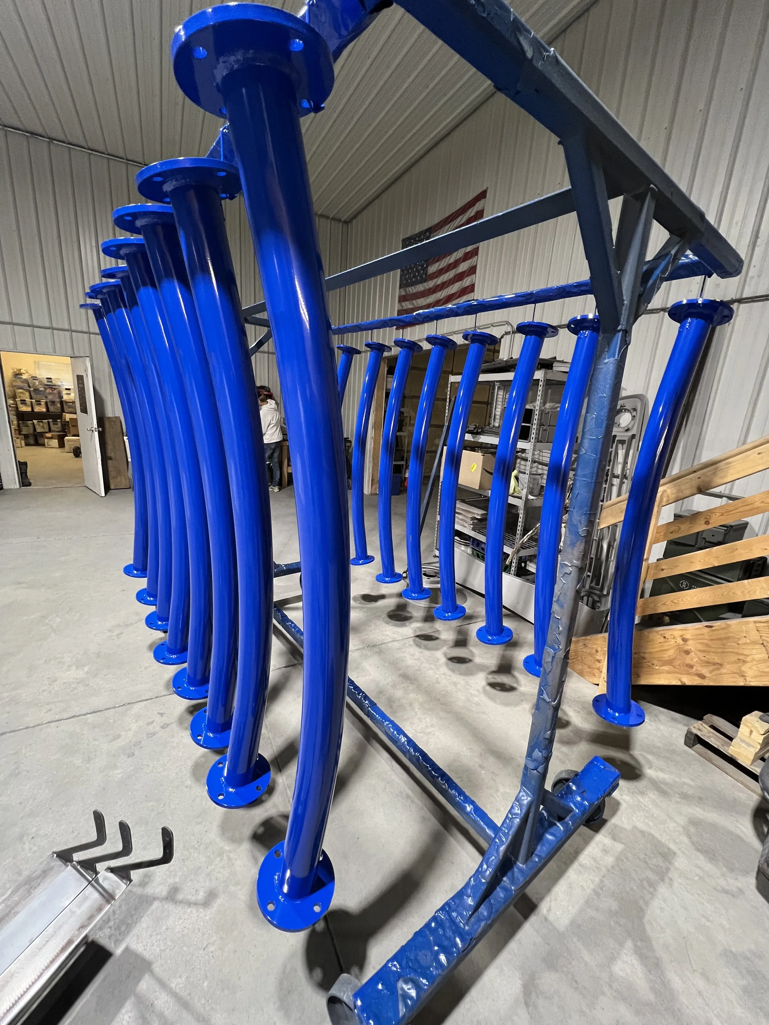 Large metal rack holding multiple blue painted metal legs or supports in a warehouse or workshop setting.