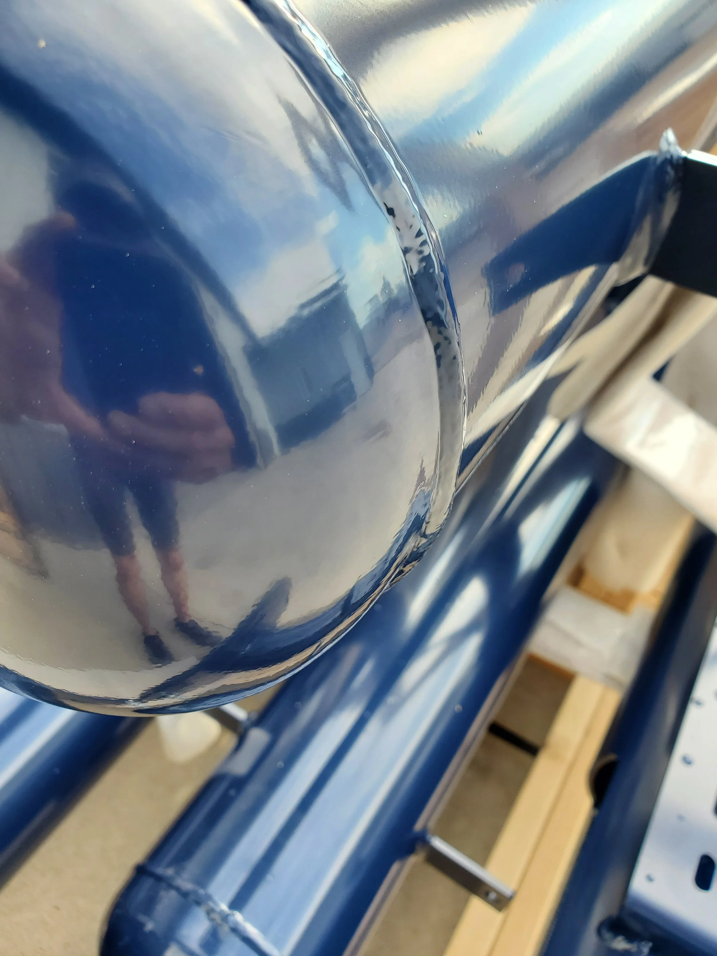 Close-up of a shiny, blue, metal machine or appliance surface with a reflection showing a person taking the photo.