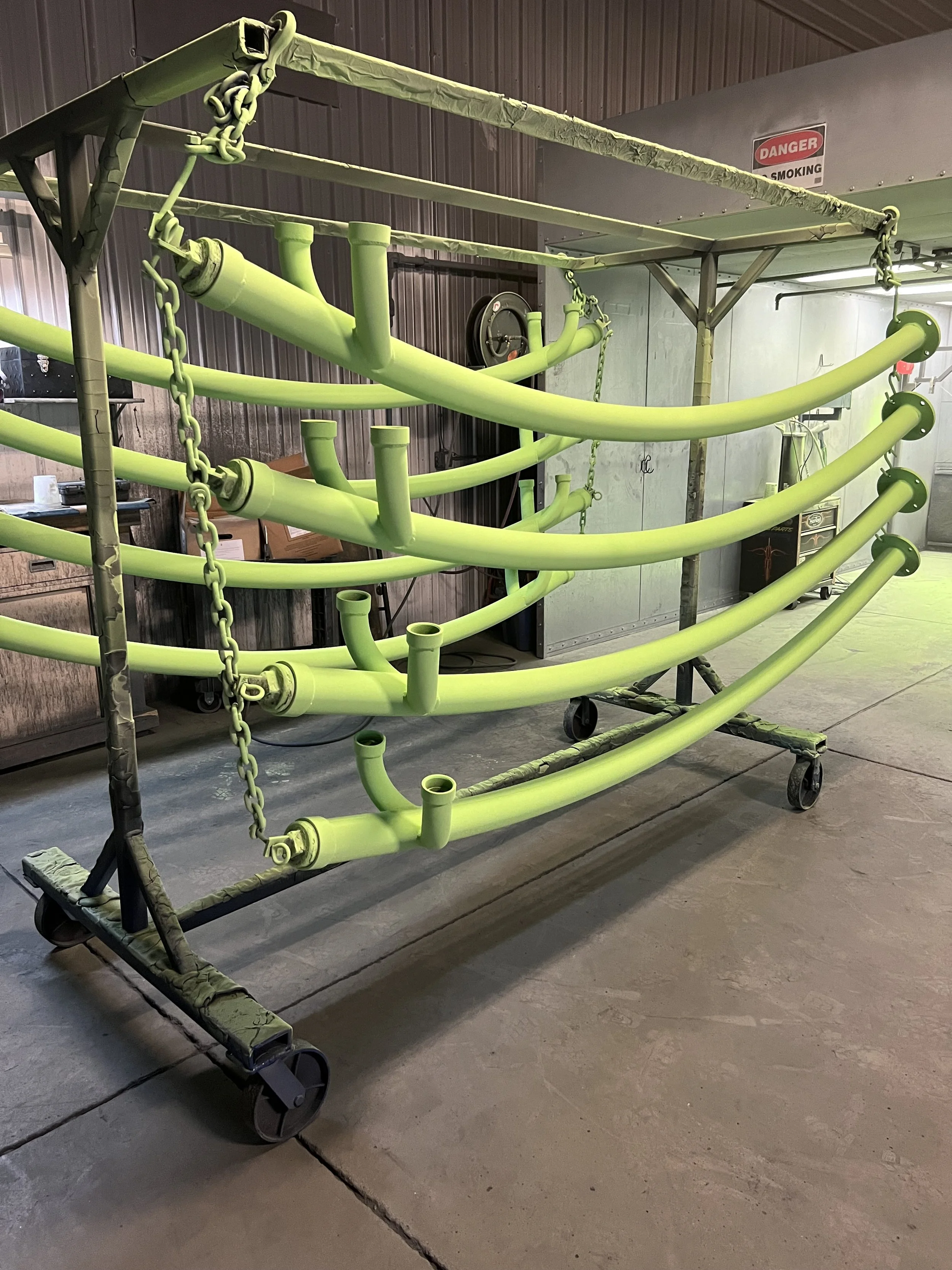 A green pipe structure on wheels inside a workshop with tools and a 'DANGER SMOKING' sign on the wall.