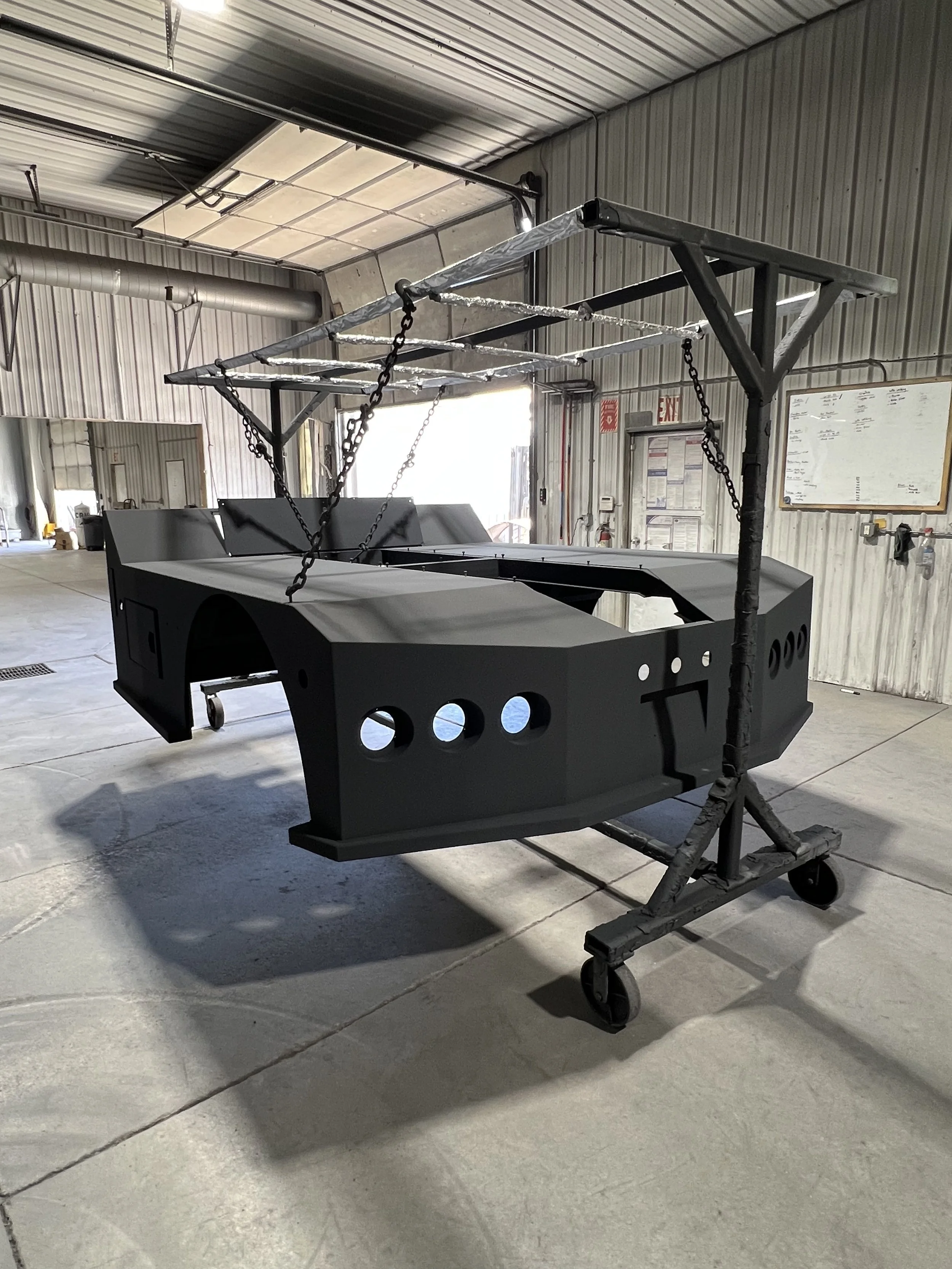 A large black vehicle frame on a mobile stand in a warehouse or workshop.