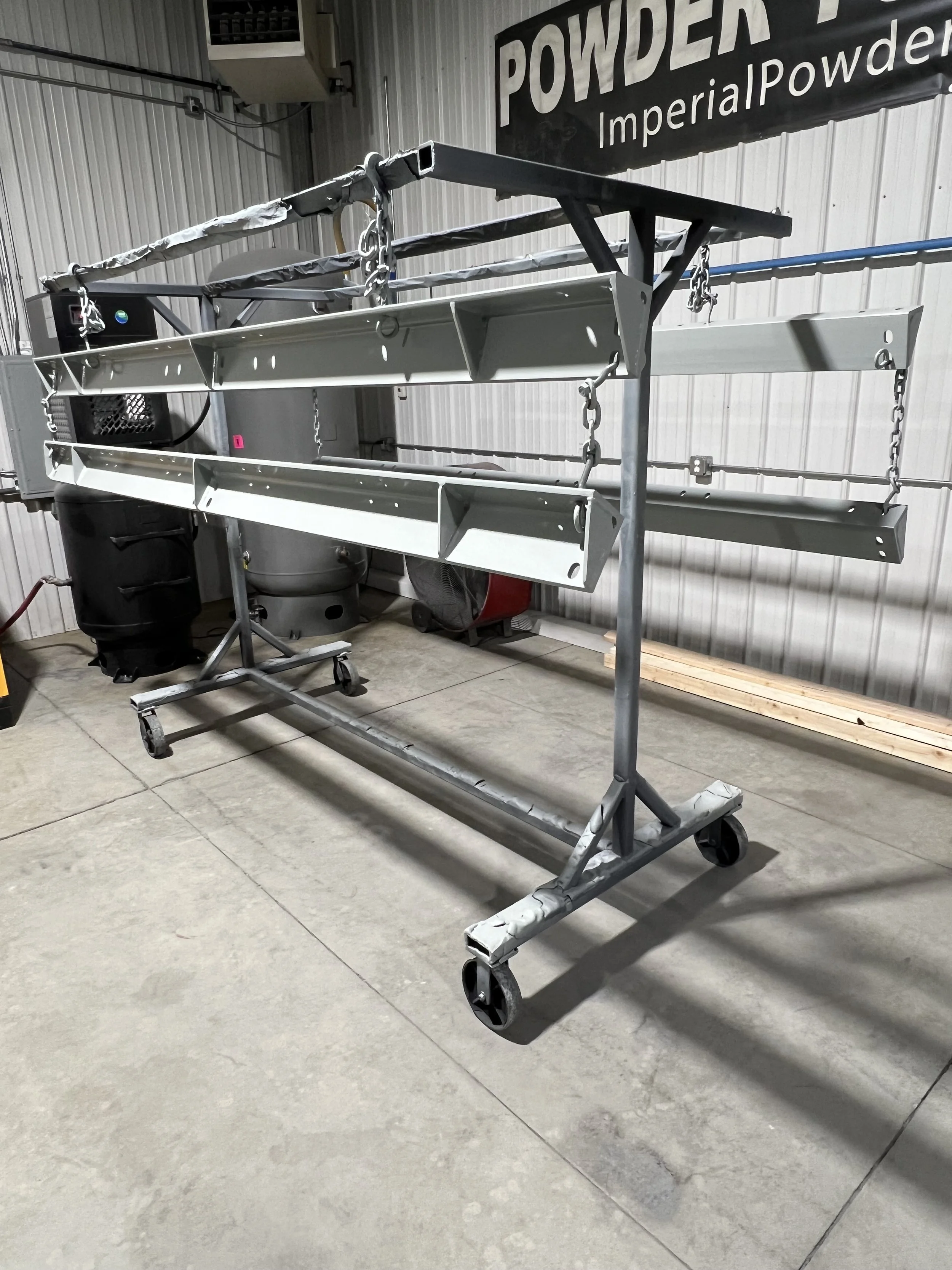 Metal scaffolding cart with wheels and chains in a warehouse, with a sign reading ' POWDER ImperialPowder' on the wall overhead.