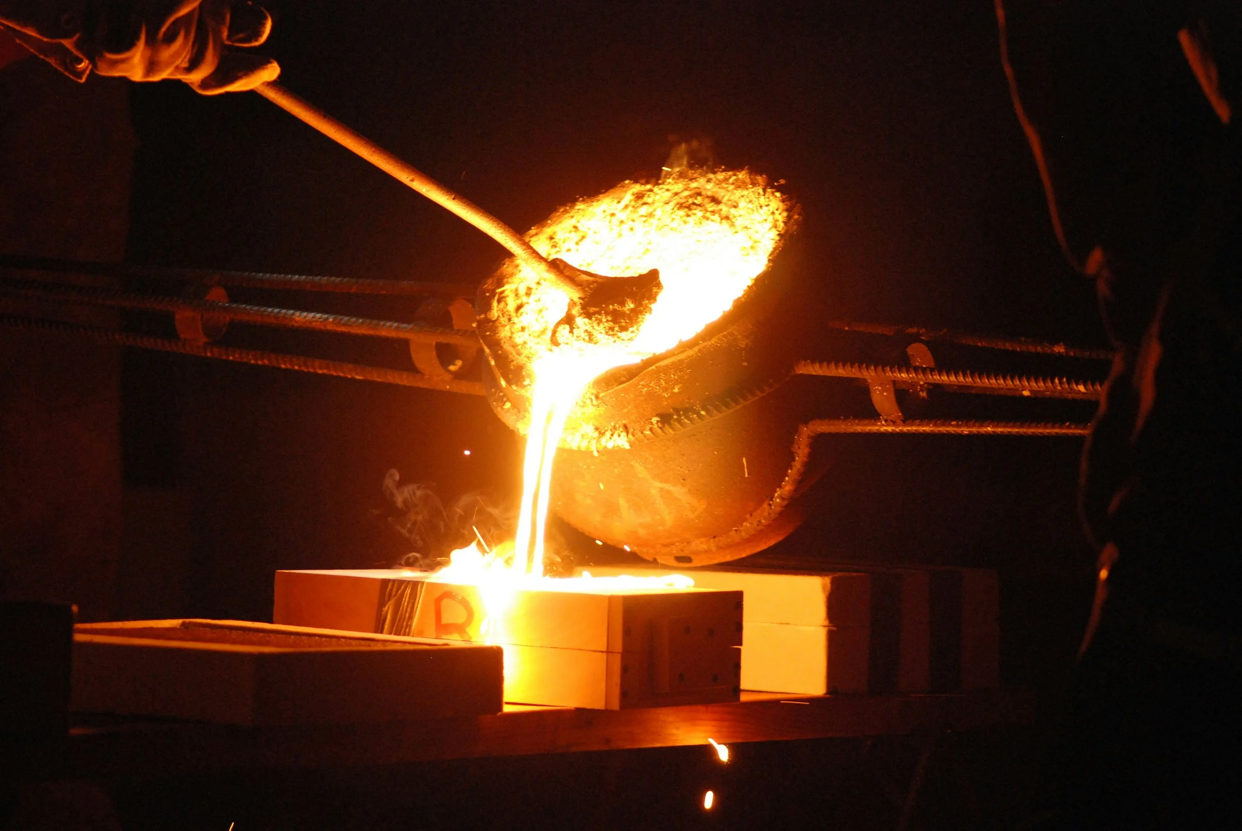 Molten metal being poured from a crucible into casting molds during the metal fabrication and foundry manufacturing process.