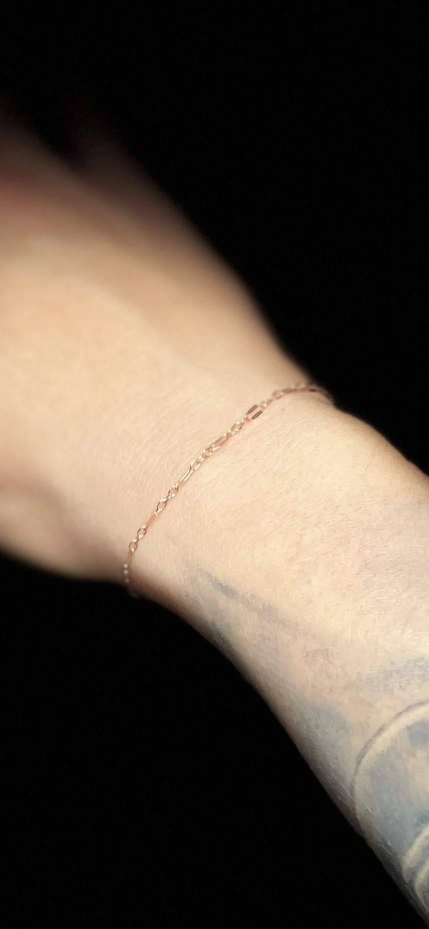 A close-up of a person's wrist wearing a delicate, thin bracelet with small links, against a dark background.
