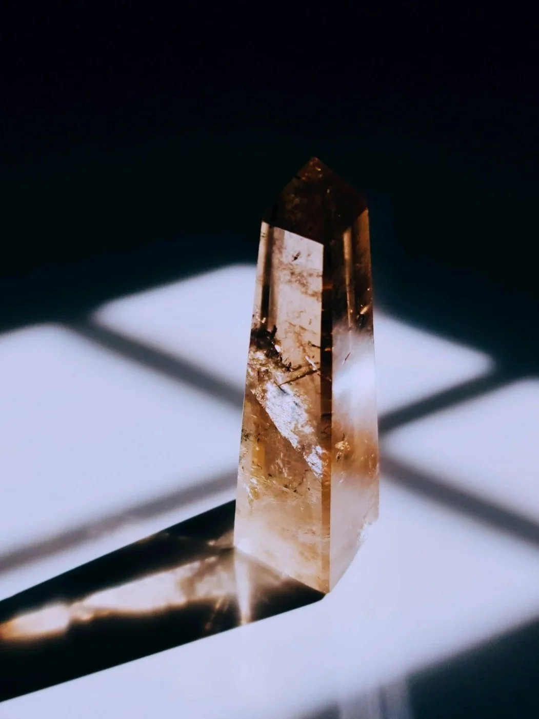 A clear, rectangular crystal casting shadows on a white surface, with a dark background.