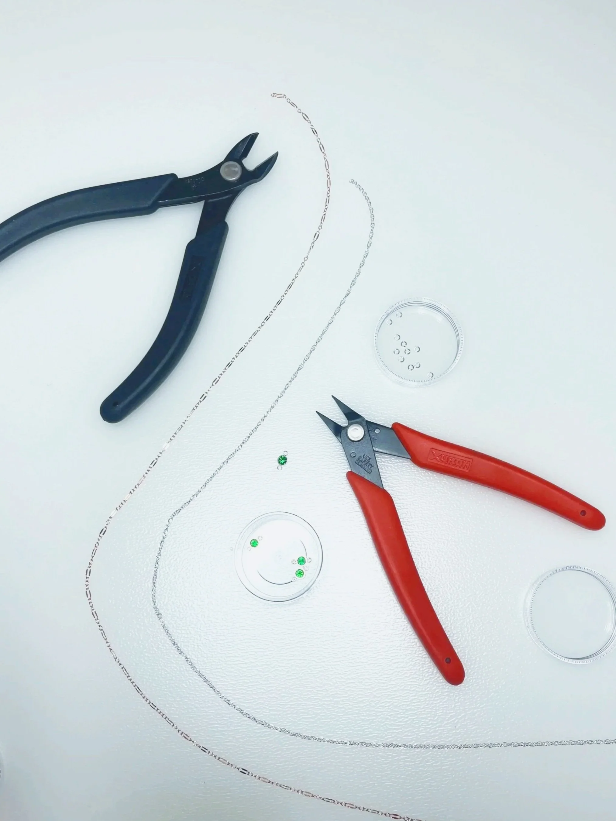 Jewelry making tools, including pliers, and small containers with beads on a white surface.