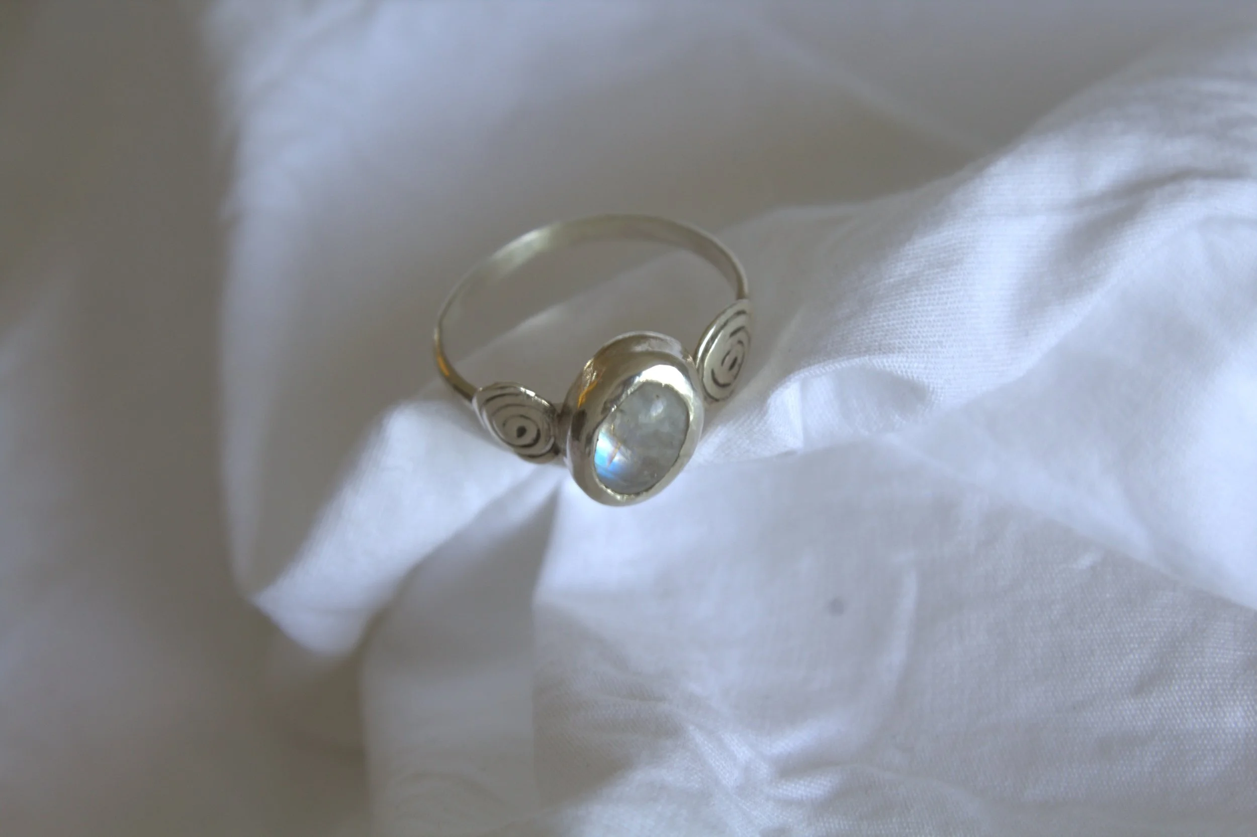 Silver ring with a large clear gemstone resting on white fabric.