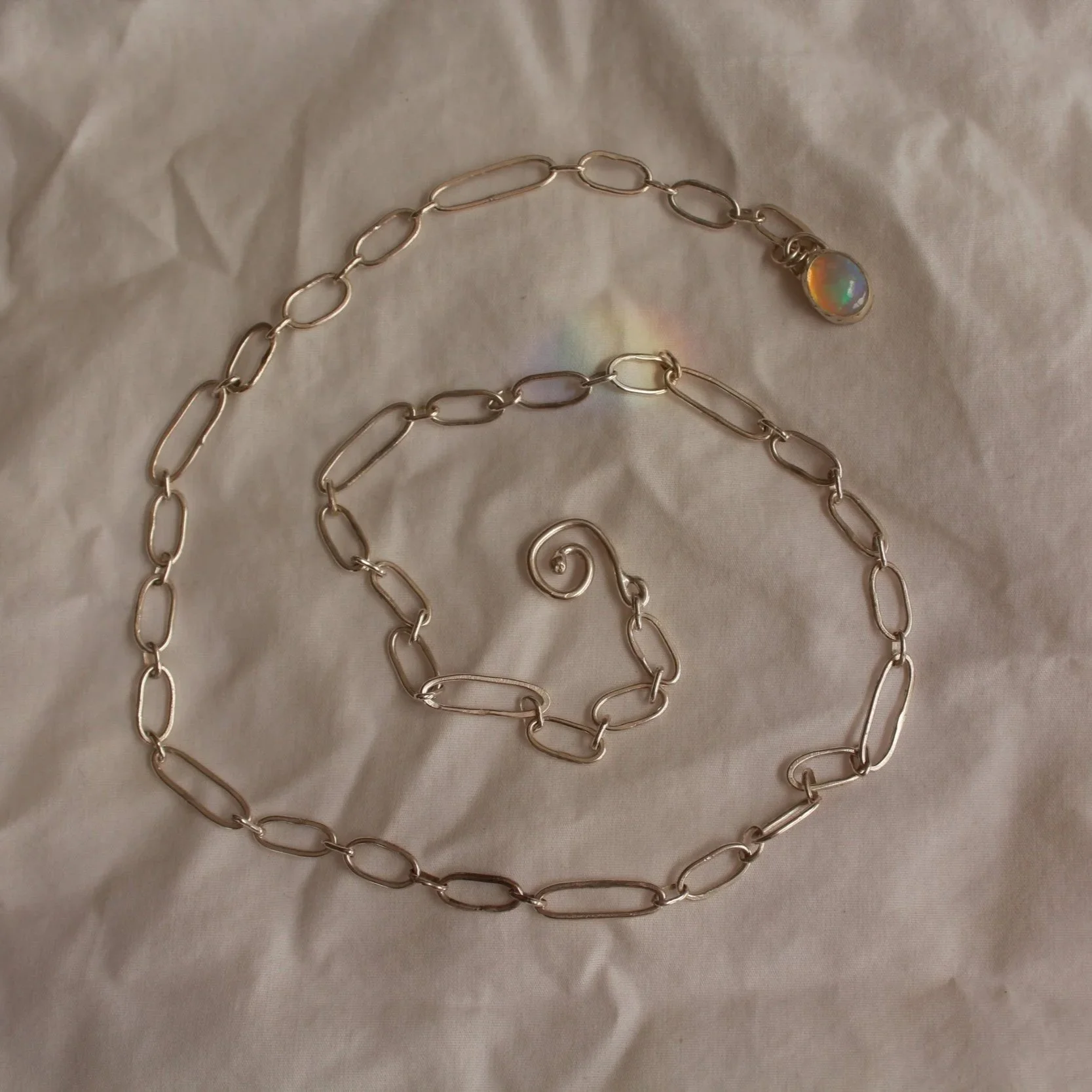 Gold chain necklace with a swirling pendant, arranged on crumpled tissue paper.