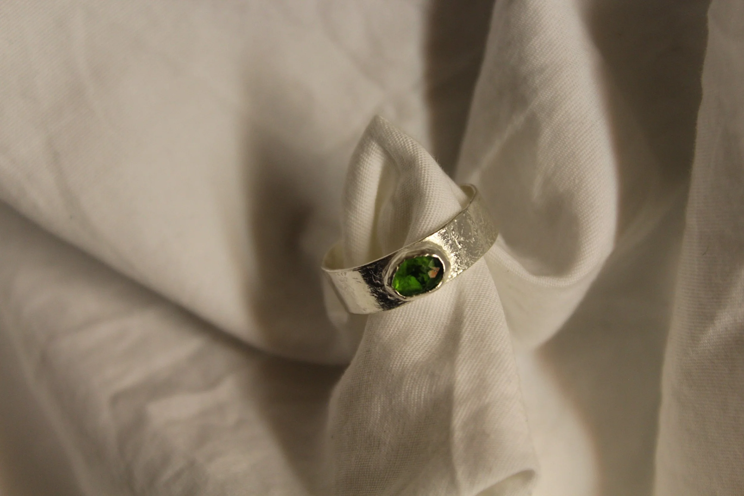 A silver ring with an oval green gemstone sitting on white fabric.