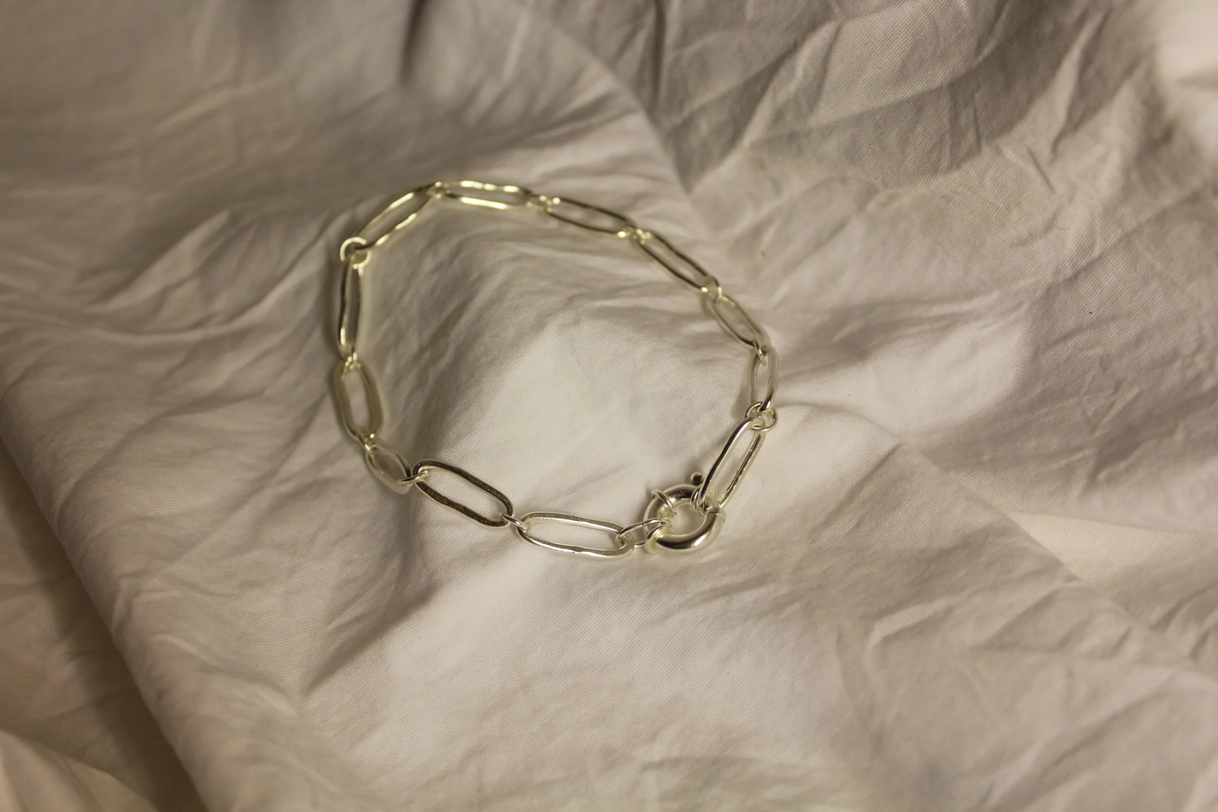 A silver chain link bracelet resting on a crinkled white fabric surface.