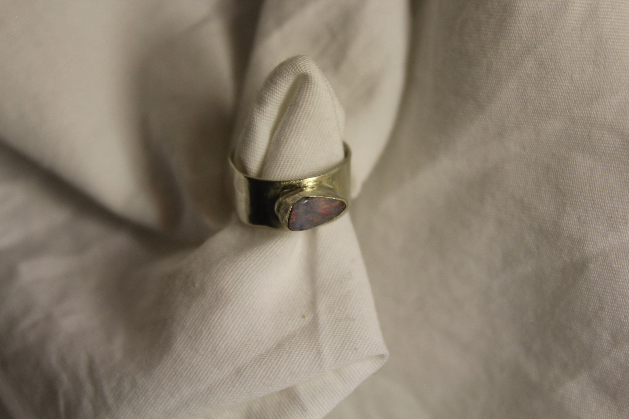 A silver ring with a dark, oval-shaped stone set in it, placed on a white fabric background.