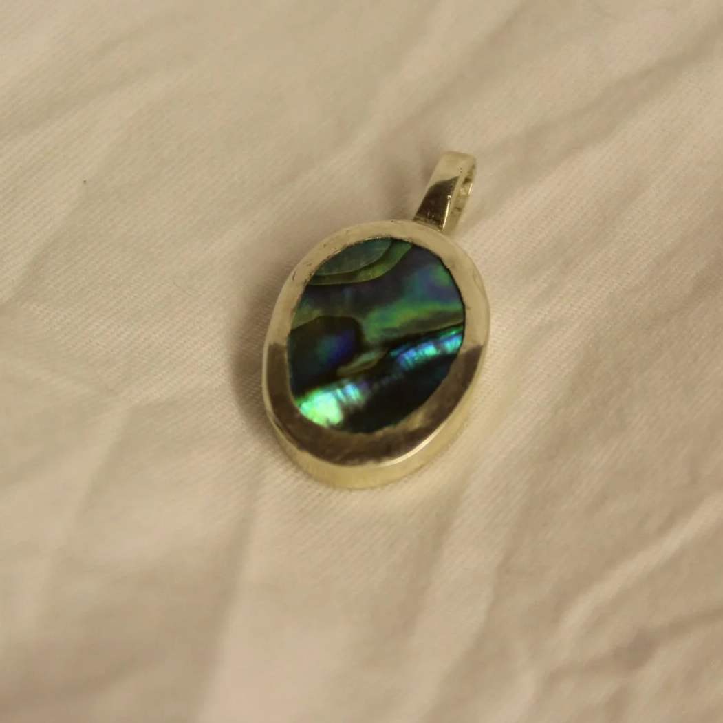 A silver ring with a large oval-shaped black and green iridescent stone, resting on a fabric surface.