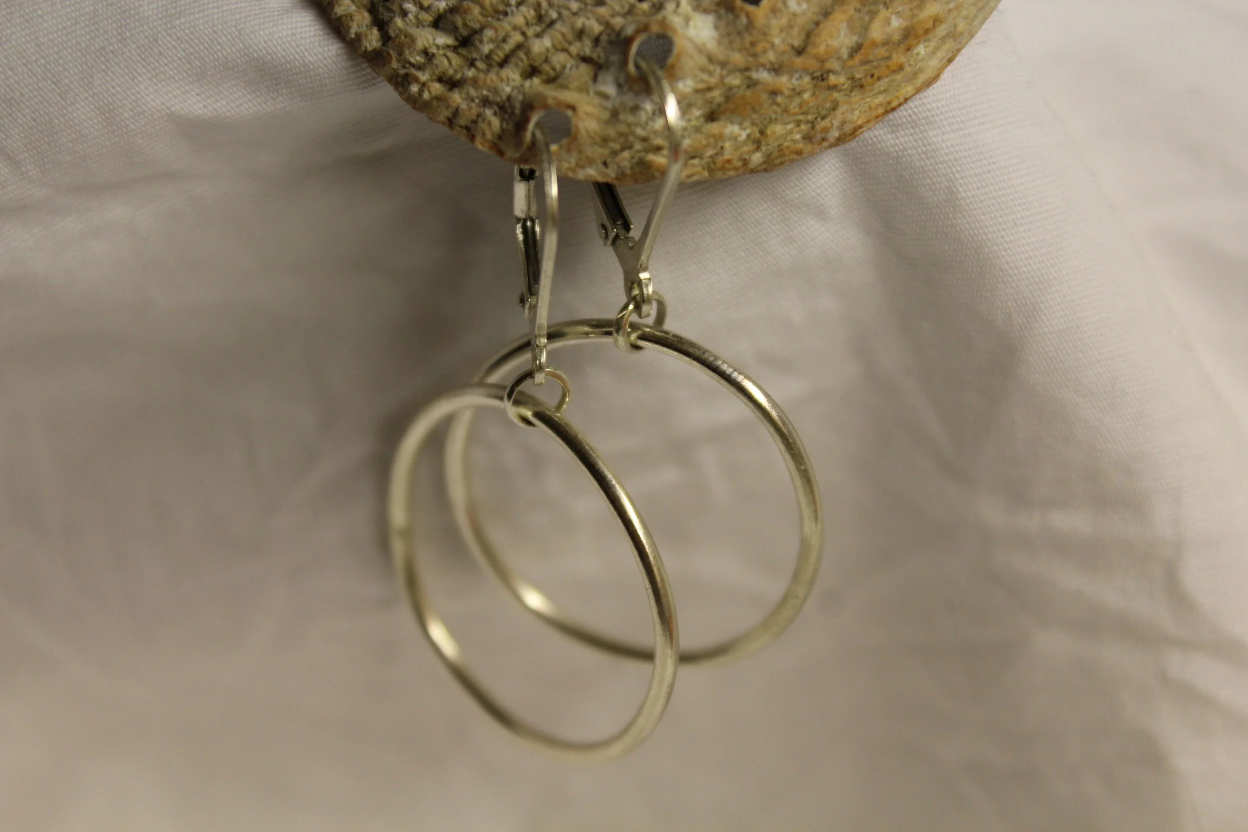 Silver hoop earrings hanging from a rock with a fabric background.