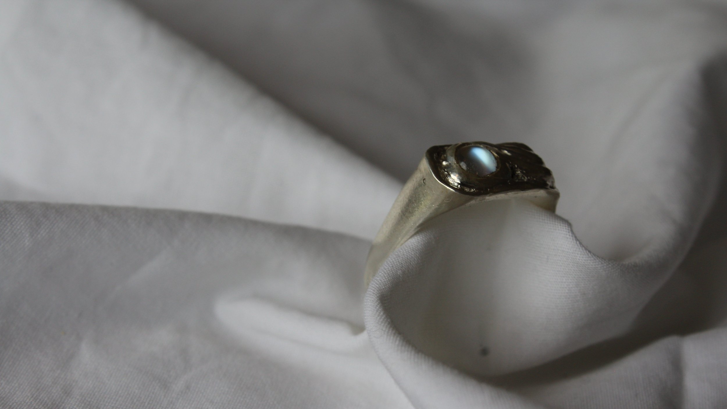 Close-up of a silver ring with a single black gemstone on a white fabric background.