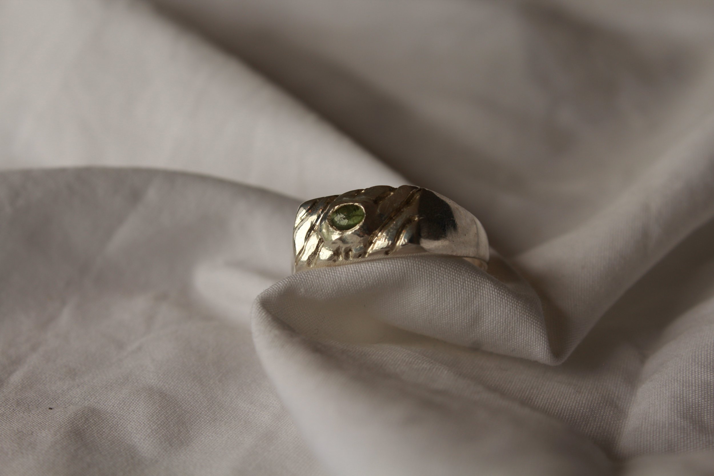 Close-up of a silver ring with a green gemstone on a white fabric surface.