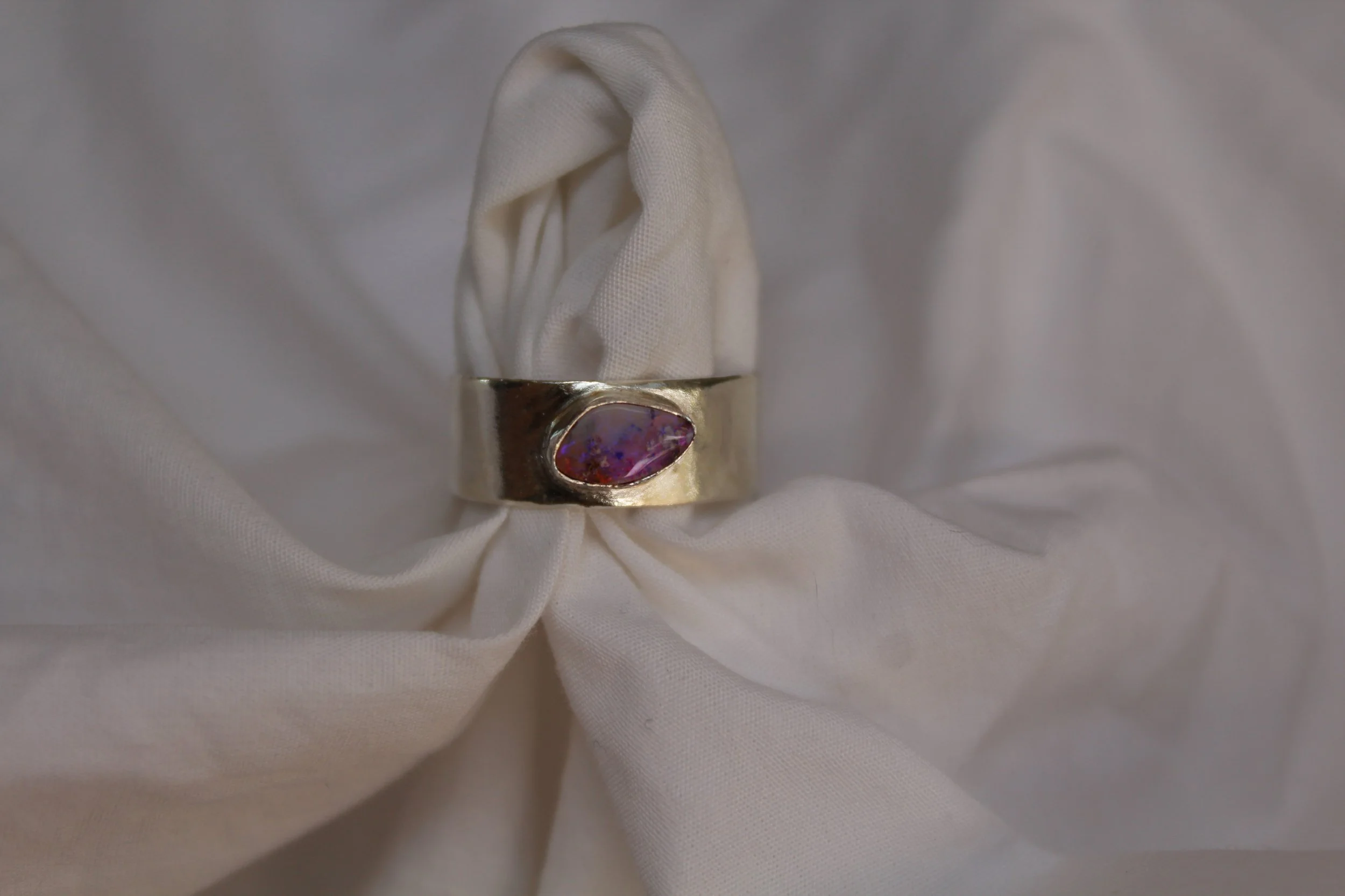 Silver ring with an oval purple and pink opal gemstone, displayed on white fabric.