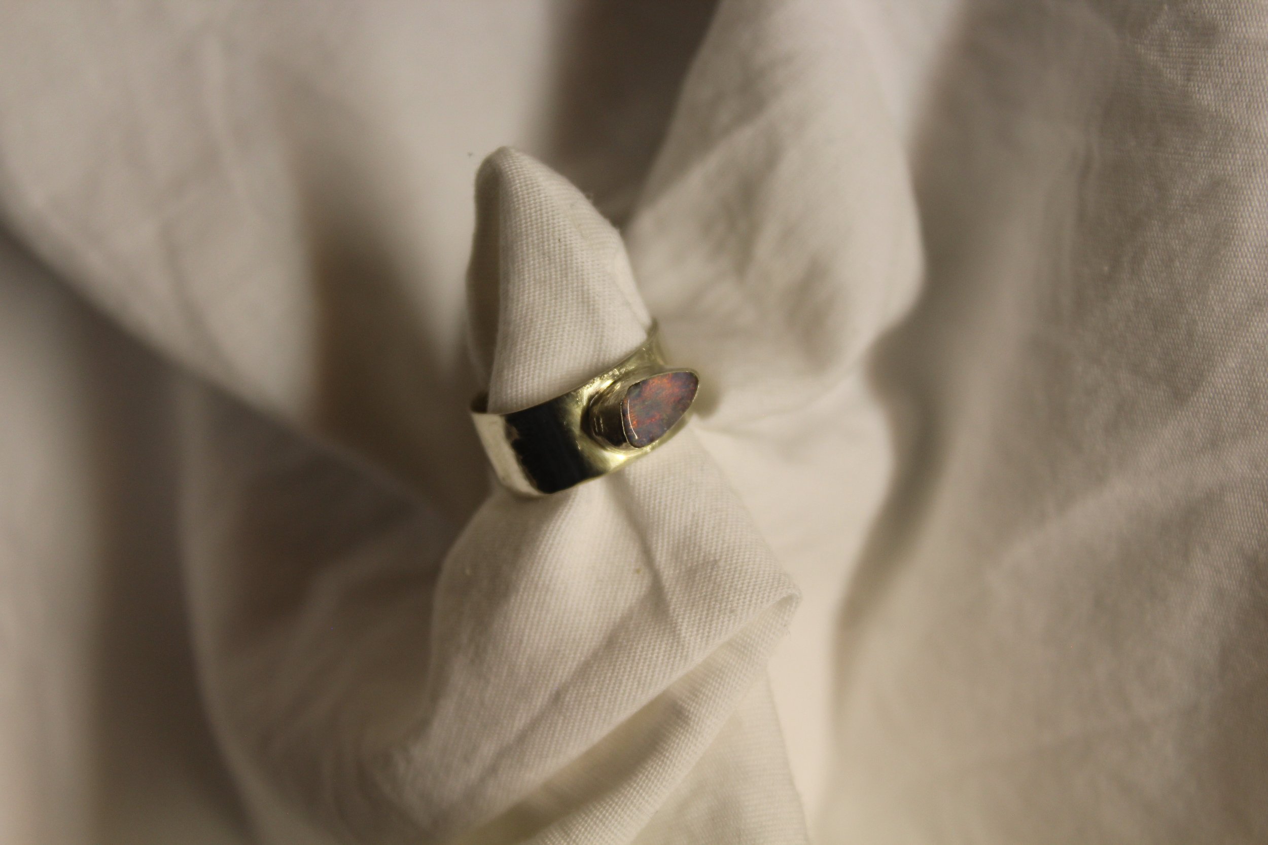 Close-up of a gold ring with a dark, oval opal stone, placed on a white fabric surface.